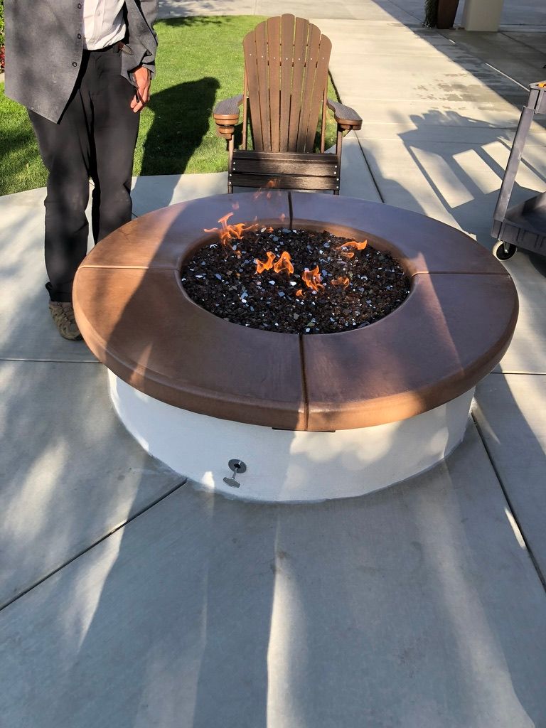 Round gas fire pit with bronze rim and black fire glass on stamped concrete patio featuring smooth broom finish