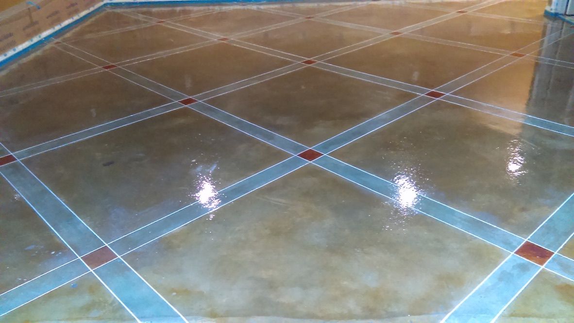 Interior stained concrete floor with diamond-pattern decorative scoring and metallic stain finish in tan tones