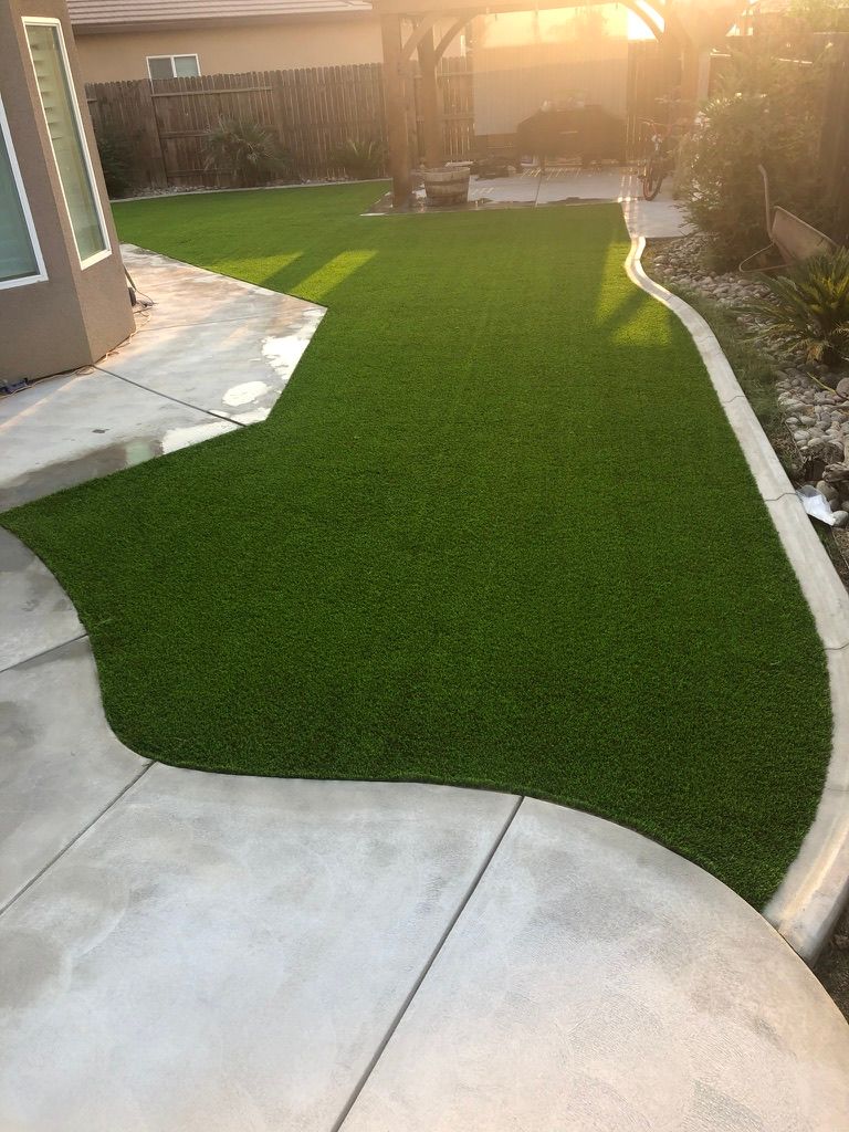 Backyard featuring artificial turf lawn with concrete patio borders, planter beds, and covered pergola