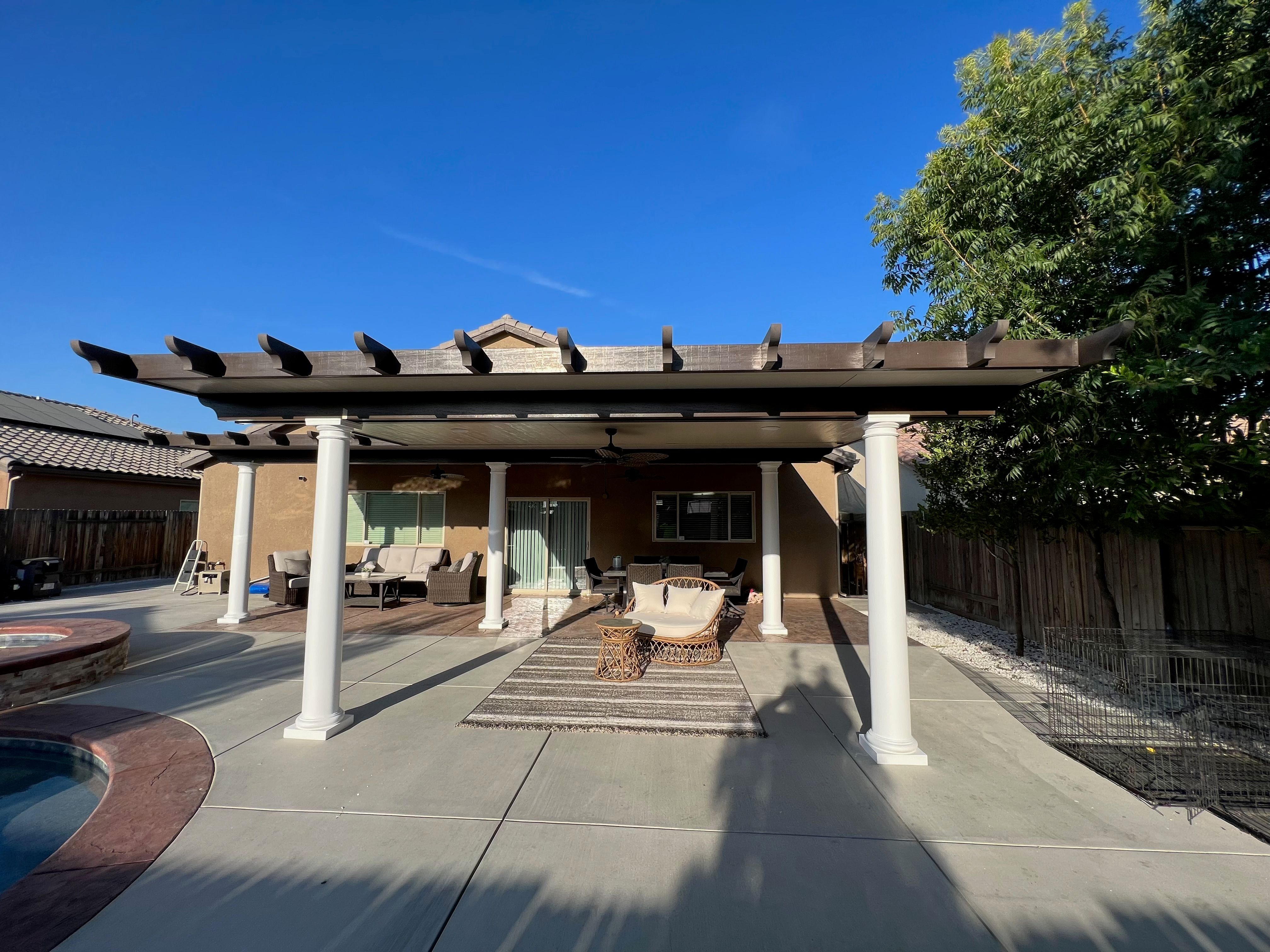 Custom pergola patio cover with dark wood beams, white columns, and stamped concrete flooring