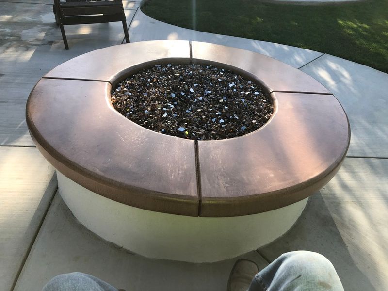 Custom gas fire pit with bronze metal rim and black fire glass on gray stamped concrete patio