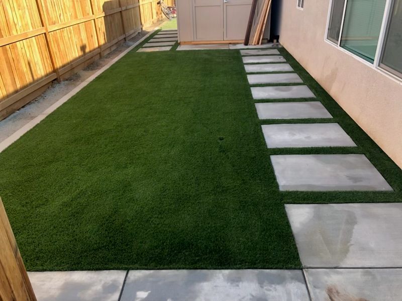 Side yard featuring artificial turf installation with large format concrete stepping pavers creating modern walkway