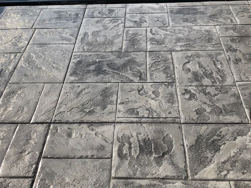 Stamped concrete patio with ashlar slate pattern in gray tones featuring textured finish and expansion joints