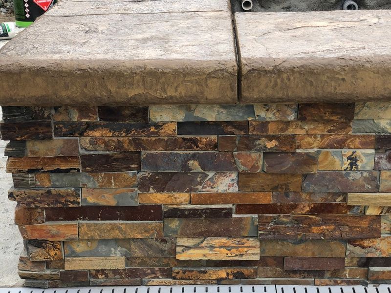 Natural multicolor stacked stone ledger veneer with rust, gold, and gray tones on concrete cap