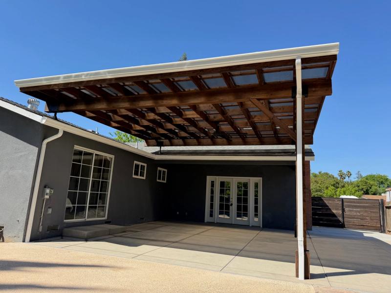 Large custom wood patio cover with translucent roof panels installed over a spacious backyard concrete patio.