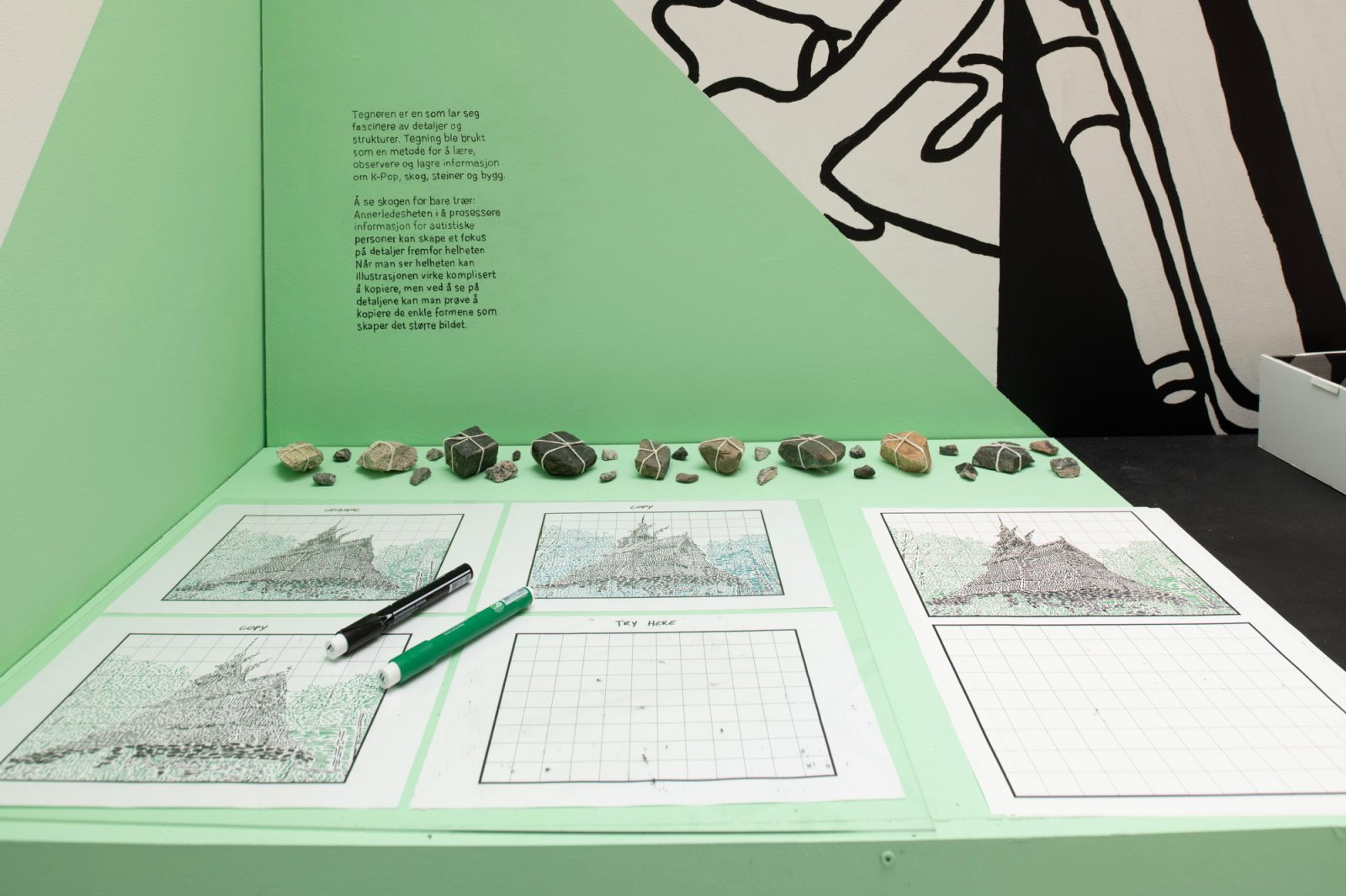 A light green interactive display with a row of rocks, grid papers showing dot-matrix landscape drawings and a blank grid, markers, and Norwegian text.