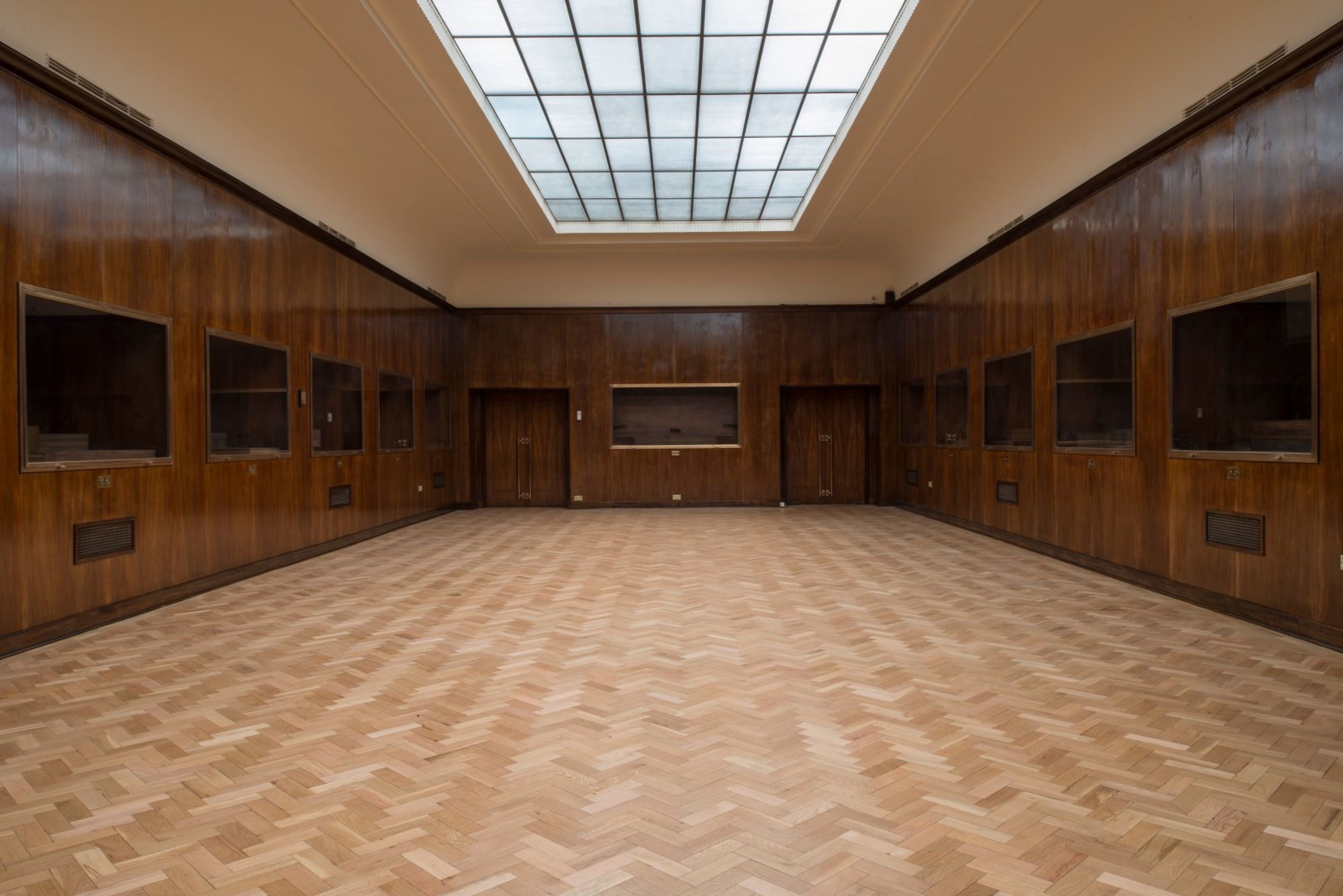 Empty room with dark wood paneling, a light herringbone wood floor, a large skylight, and built-in display cases.