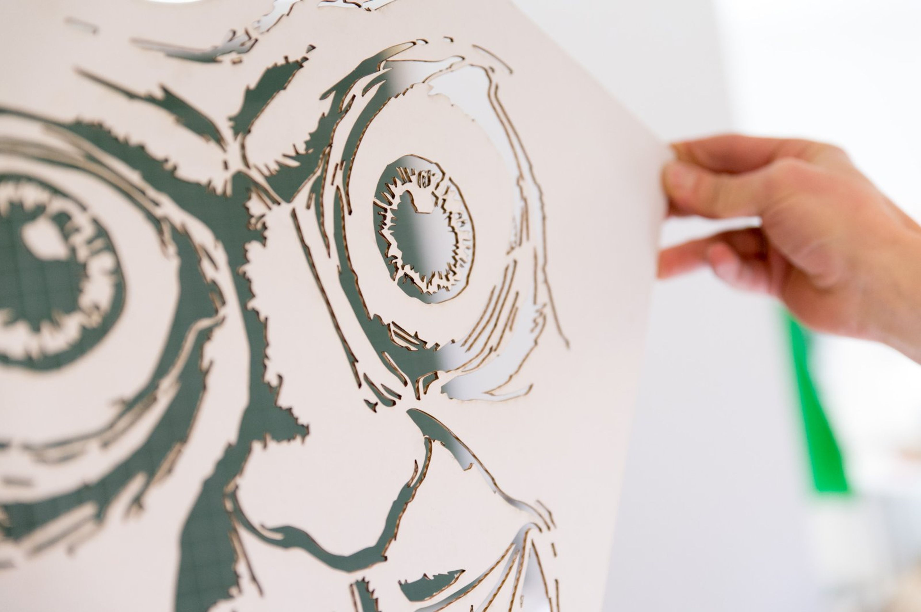 Hand holding up a sheet of paper with an intricate laser-cut design of eyes.