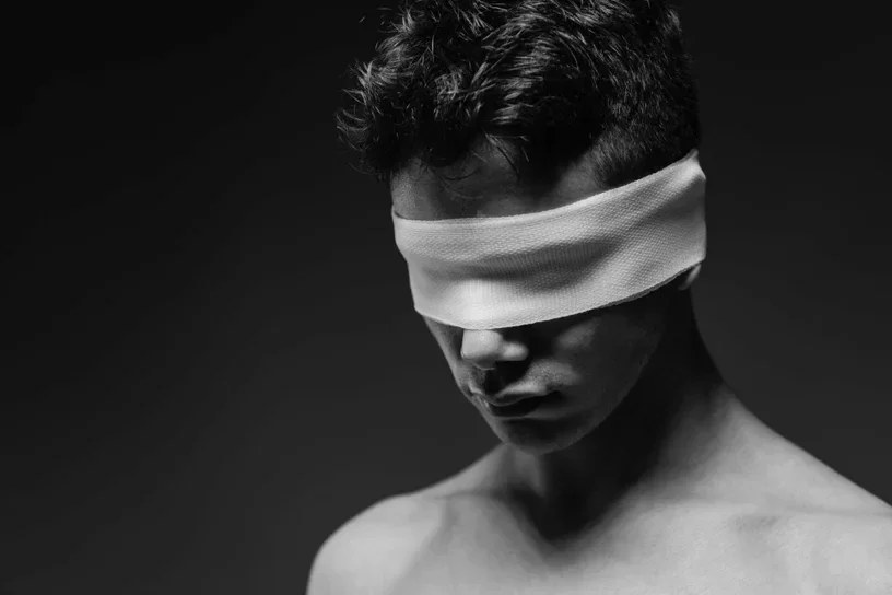 A striking black and white fine art photograph by Arjan Spannenburg from the Blind Love series, featuring a shirtless man wearing a white blindfold, symbolizing the conceptual intersection of trust, vulnerability, and surrender.