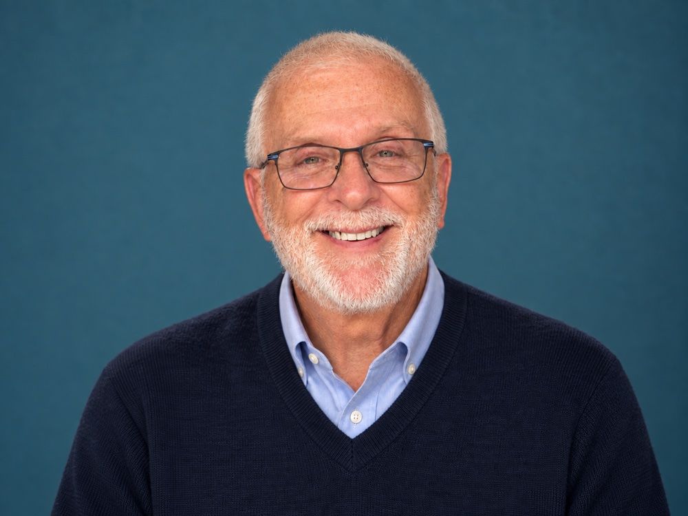Dr. Terry D. Burger smiling, with white hair, a beard and glasses, wearing a navy sweater over a light blue shirt