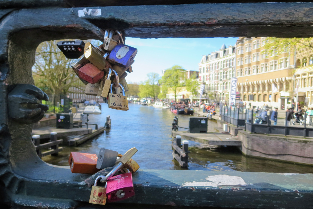 Padlocks fastened to a bridge railing overlooking an Amsterdam canal