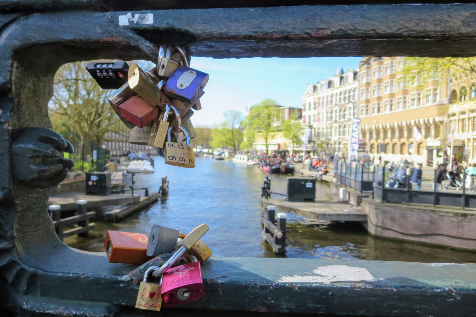 Padlocks fastened to a bridge railing overlooking an Amsterdam canal