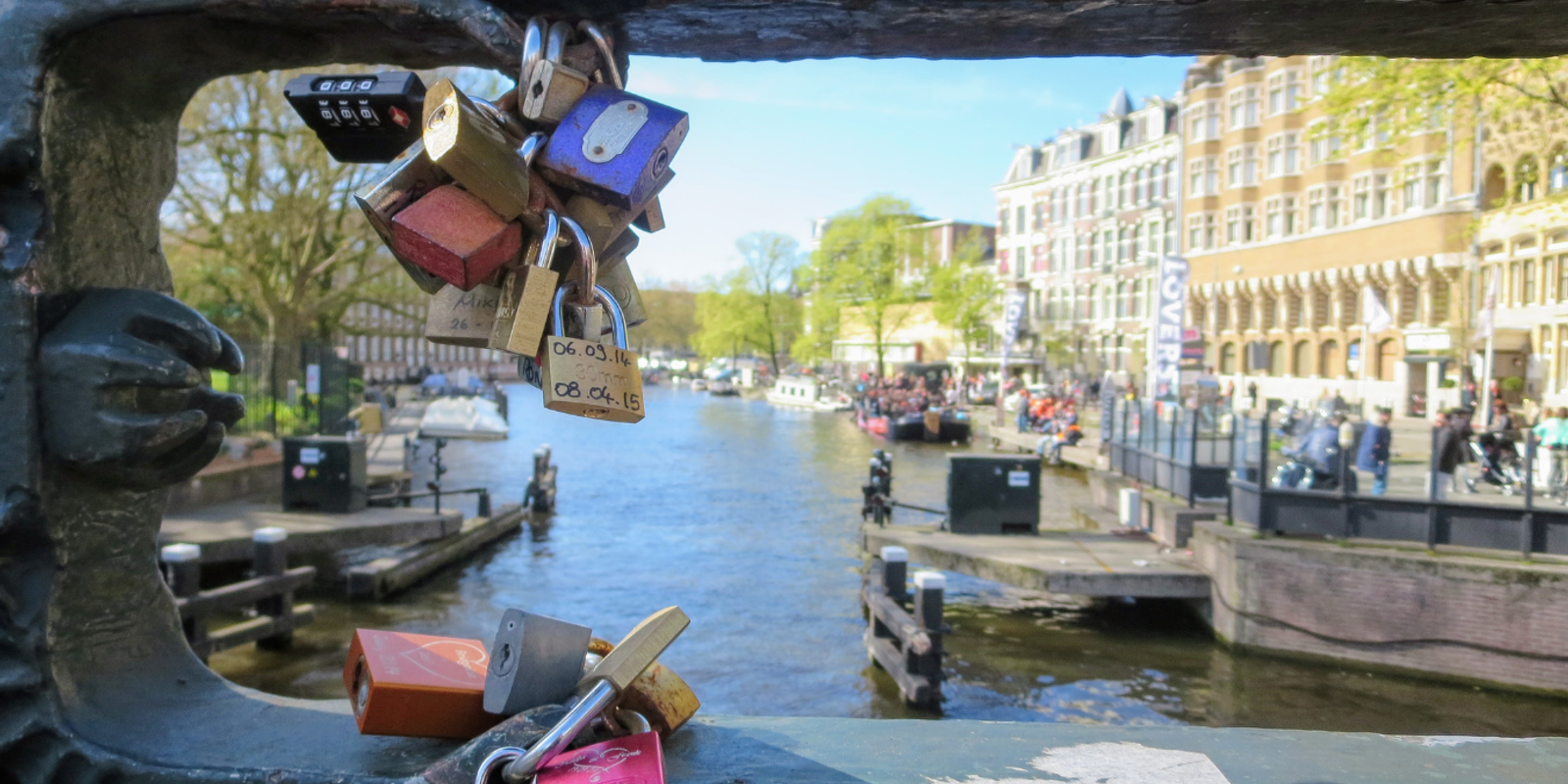 Padlocks fastened to a bridge railing overlooking an Amsterdam canal