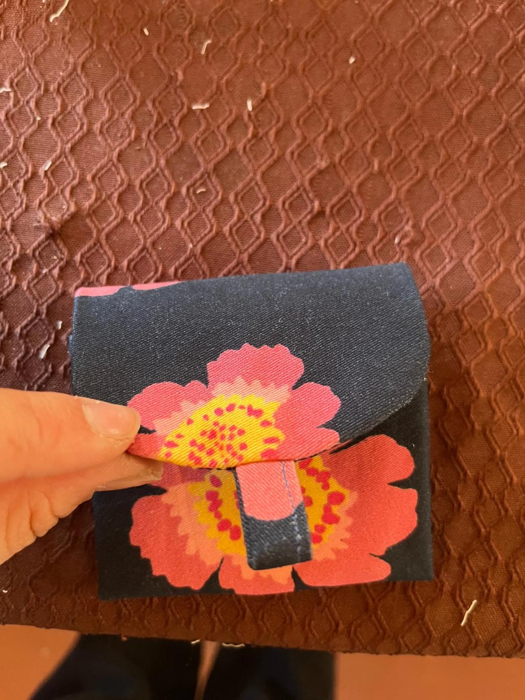 Petite pochette en tissu bleu marine à grandes fleurs roses et jaunes, tenue en main.