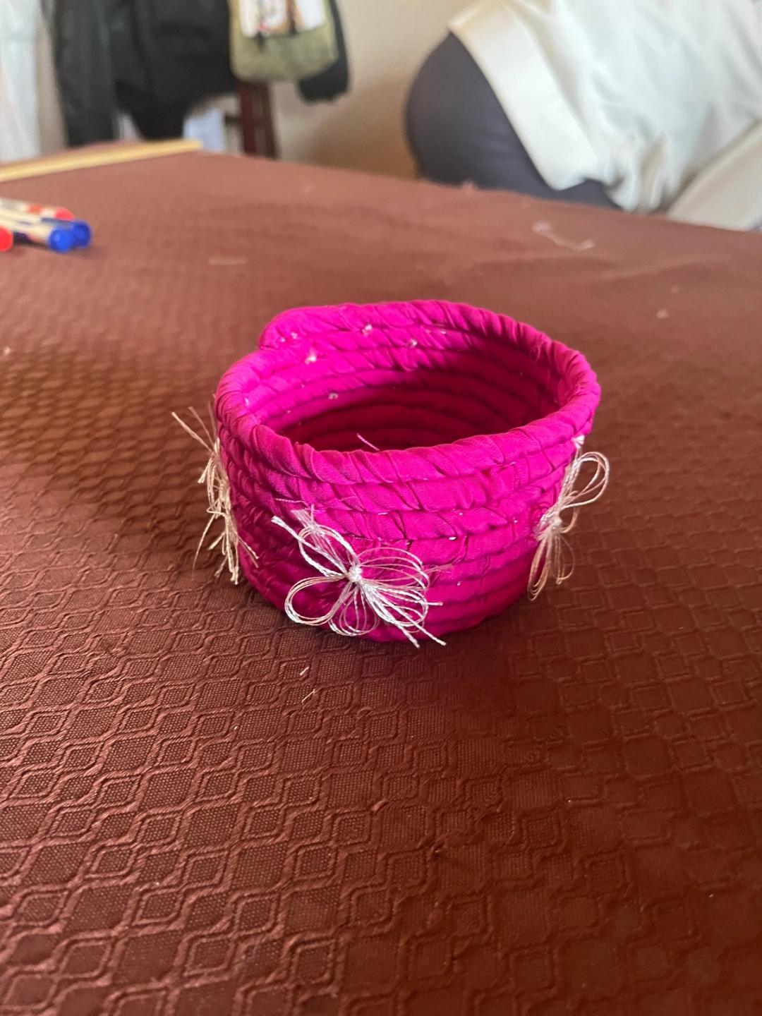 Petit panier en tissu enroulé rose fuchsia, décoré de nœuds de fil blanc.