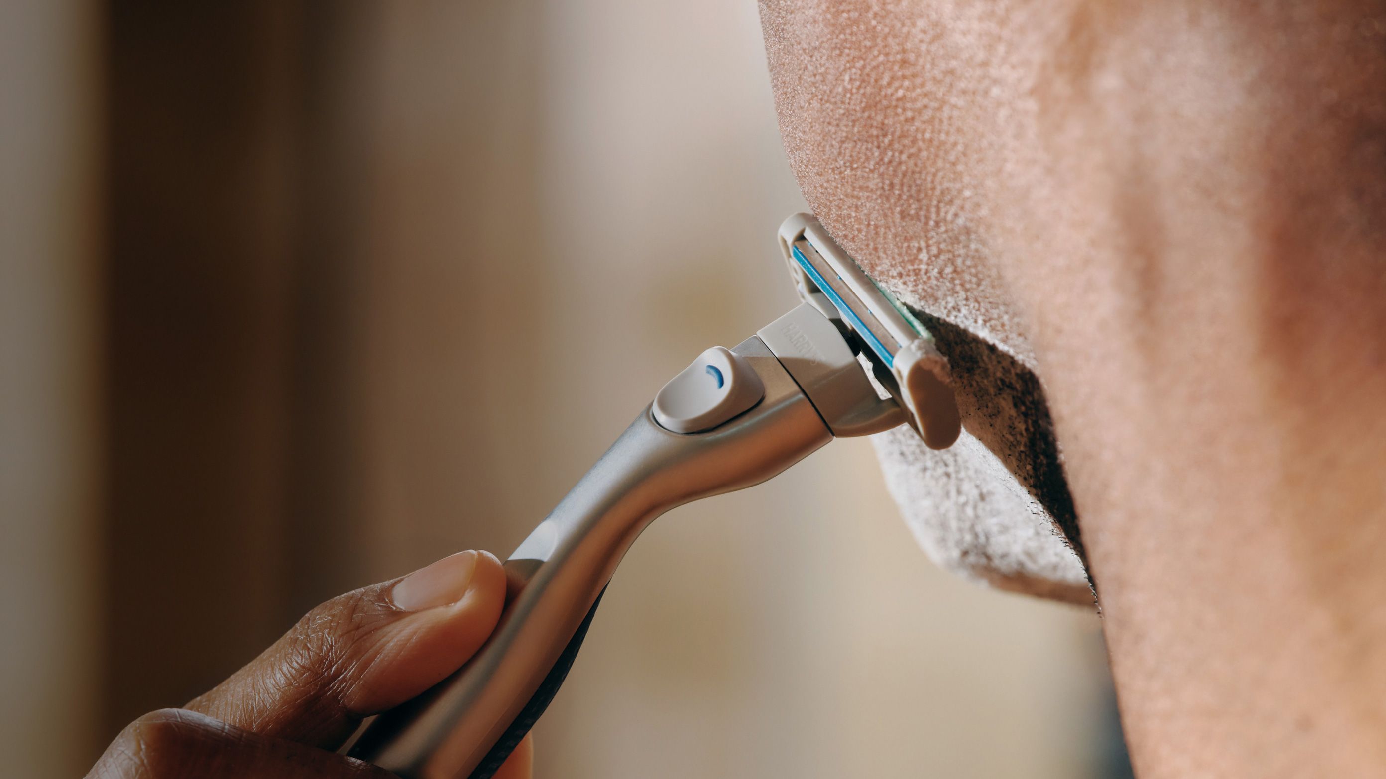 Man shaving his face with Harry's Plus razor against a blurred background