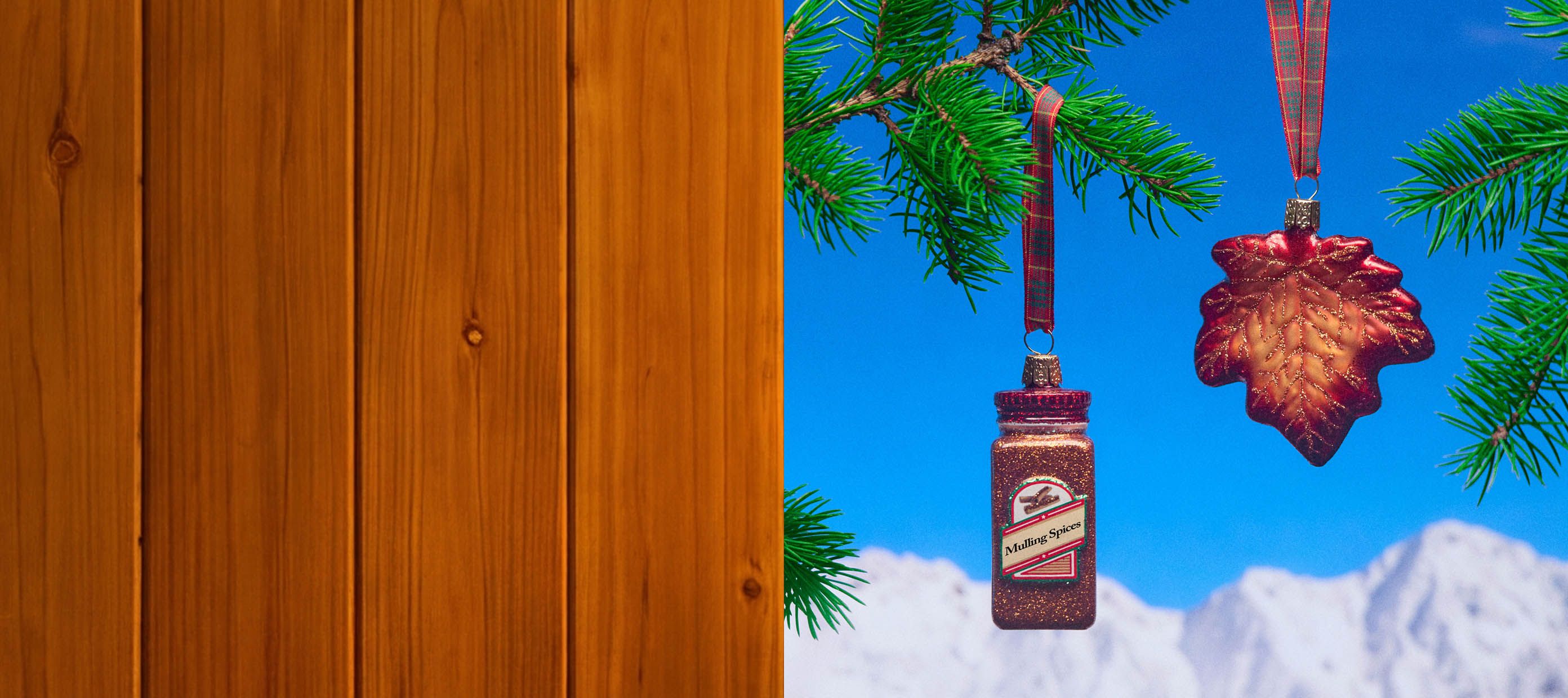 Wood panels on the left with maple and spice seasoning themed ornaments on a blue sky and mountain background on the right with a few pine branches surrounding the ornaments.