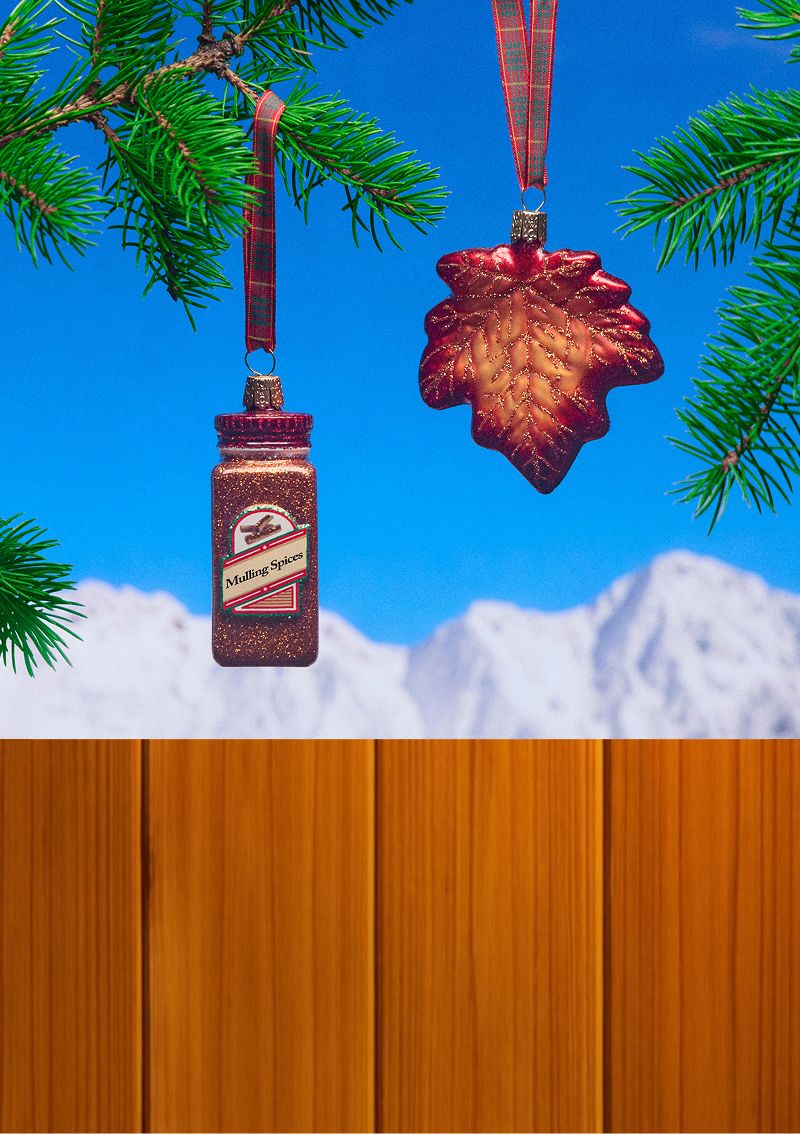 Wood panels on the left with maple and spice seasoning themed ornaments on a blue sky and mountain background on the right with a few pine branches surrounding the ornaments.
