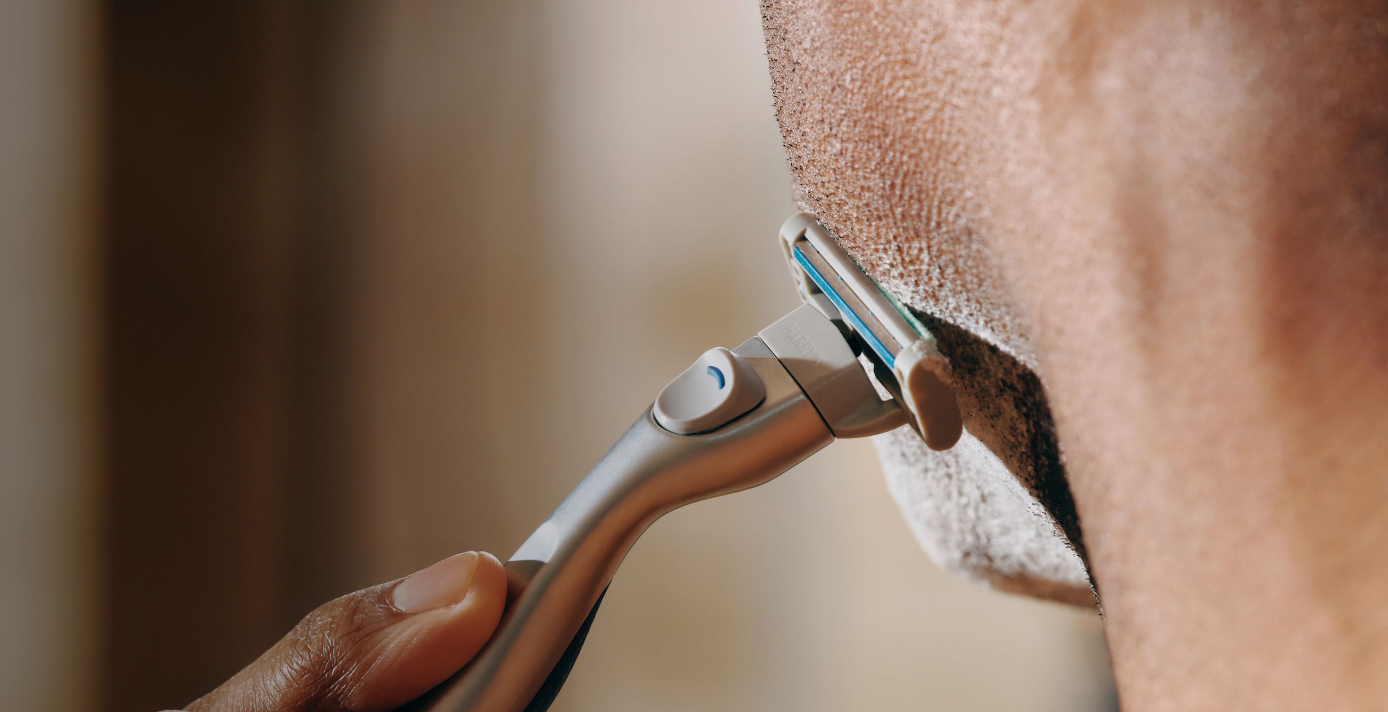 Man shaving his face with Harry's Plus razor against a blurred background