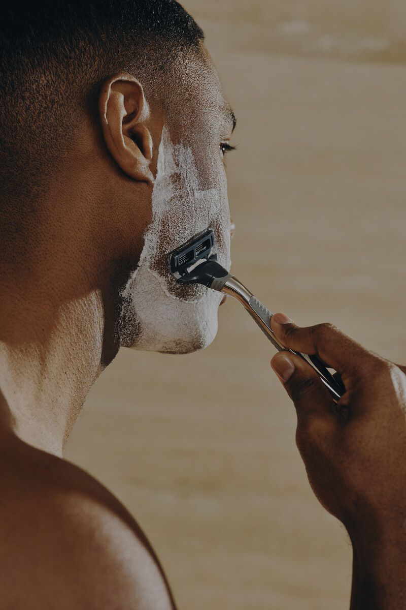 A view from the side of a man shaving his face in a bathroom
