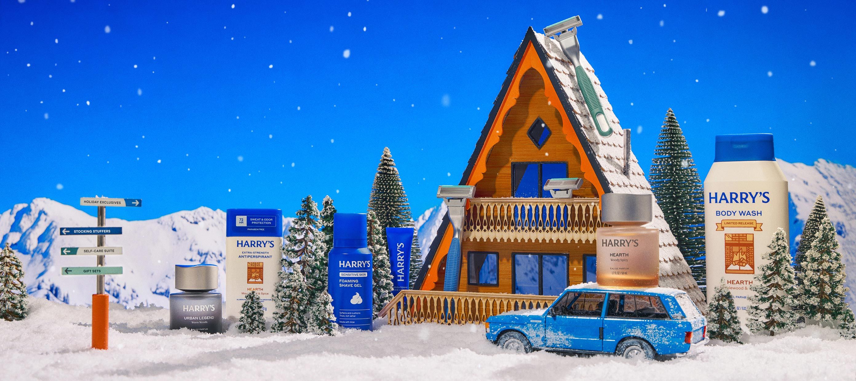 An alpine setting with an A-frame house and blue station wagon parked out front with pine trees and mountains and snow with Harrry's holiday products strewn around the setting in the manner of a diorama