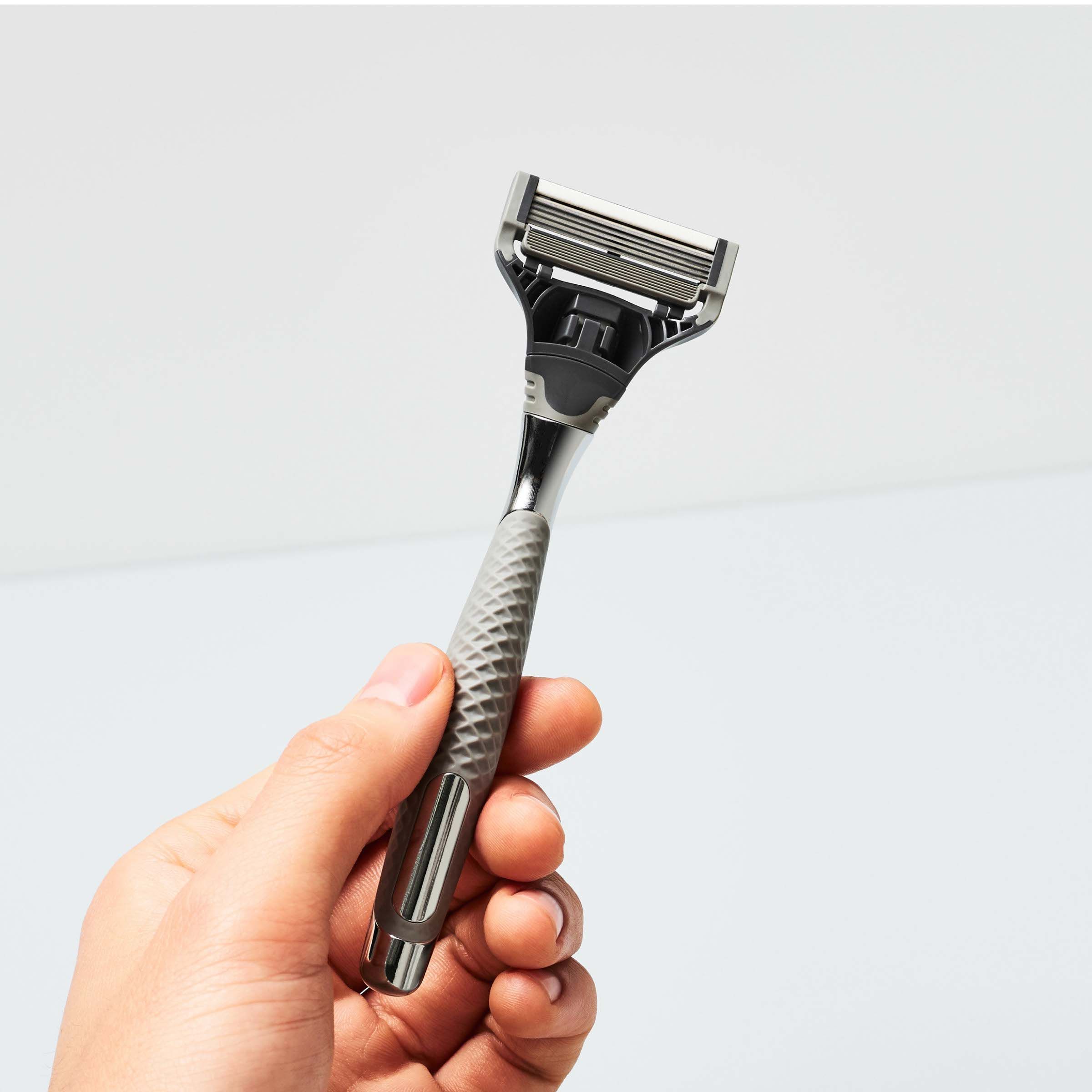 Hand holding the Winston razor, facing upward to show the five-blade cartridge and rubberized grip.
