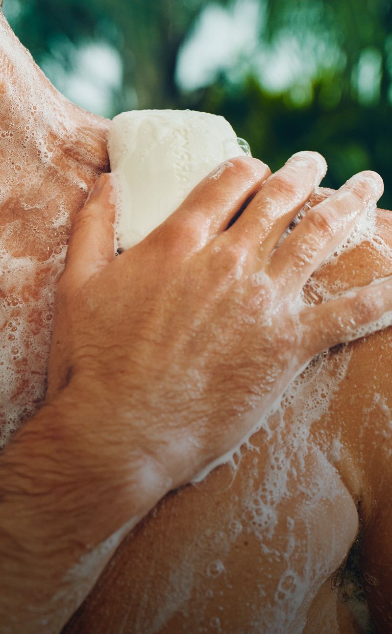 Close-up of a man's hand using bar soap on his sholder with soap suds.
