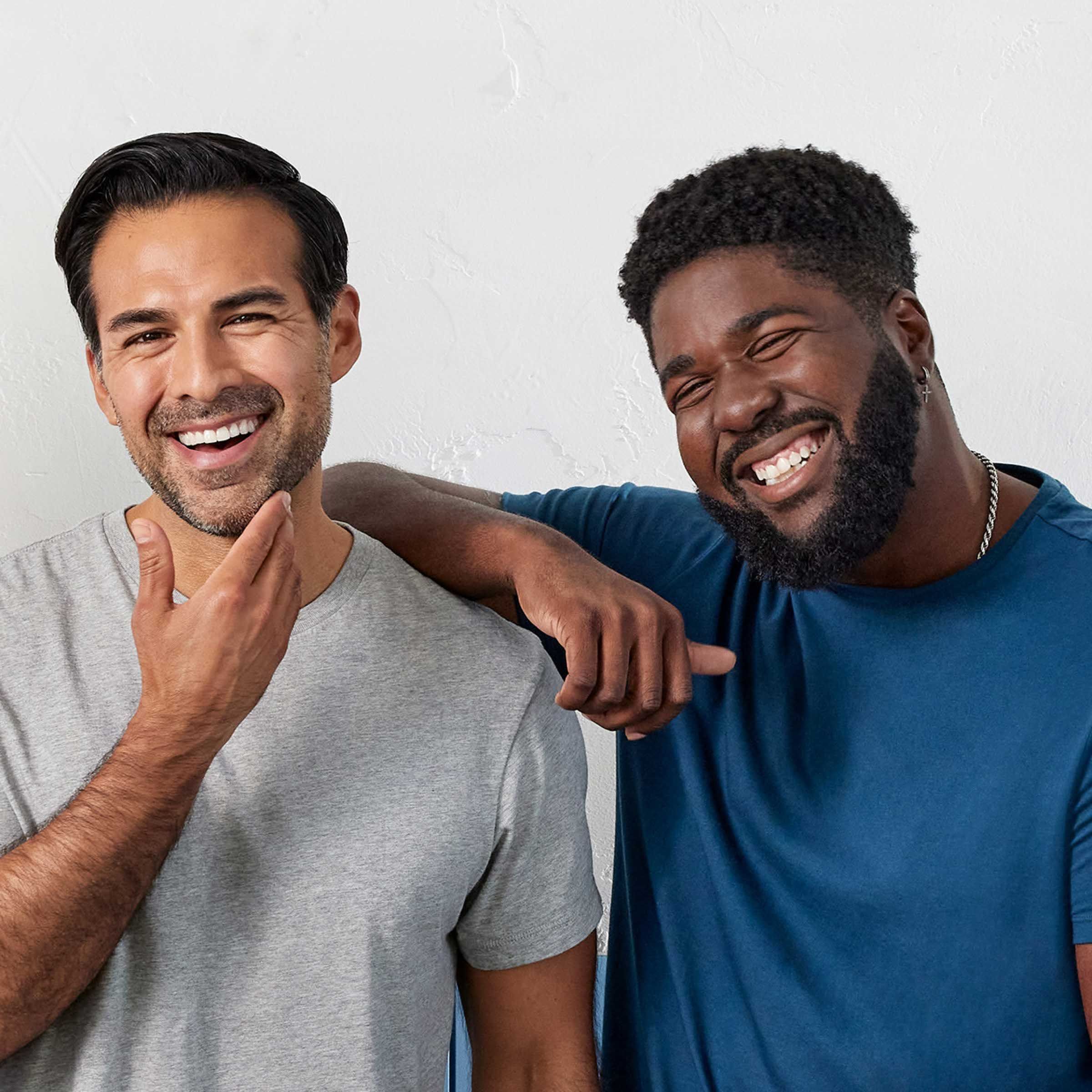 Two men with facial hair, standing side by side laughing together.
