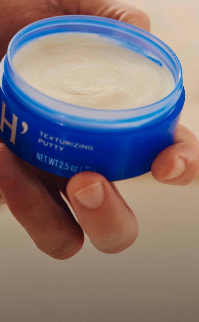 Jar of open Harry's Texturizing Putty held by a hand.