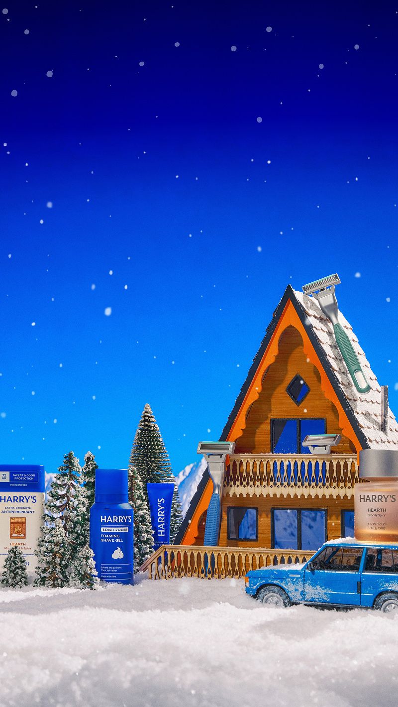 An alpine setting with an A-frame house and blue station wagon parked out front with pine trees and mountains and snow with Harrry's holiday products strewn around the setting in the manner of a diorama