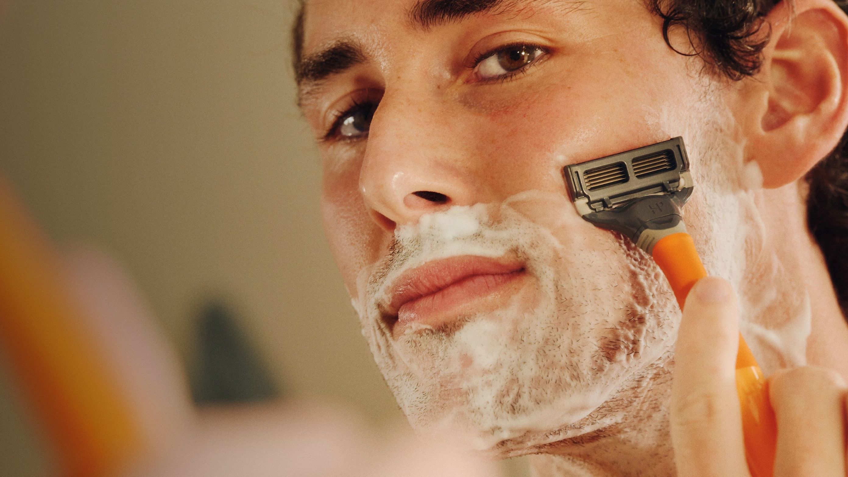 Front of man's face showing him shaving against a blurry background