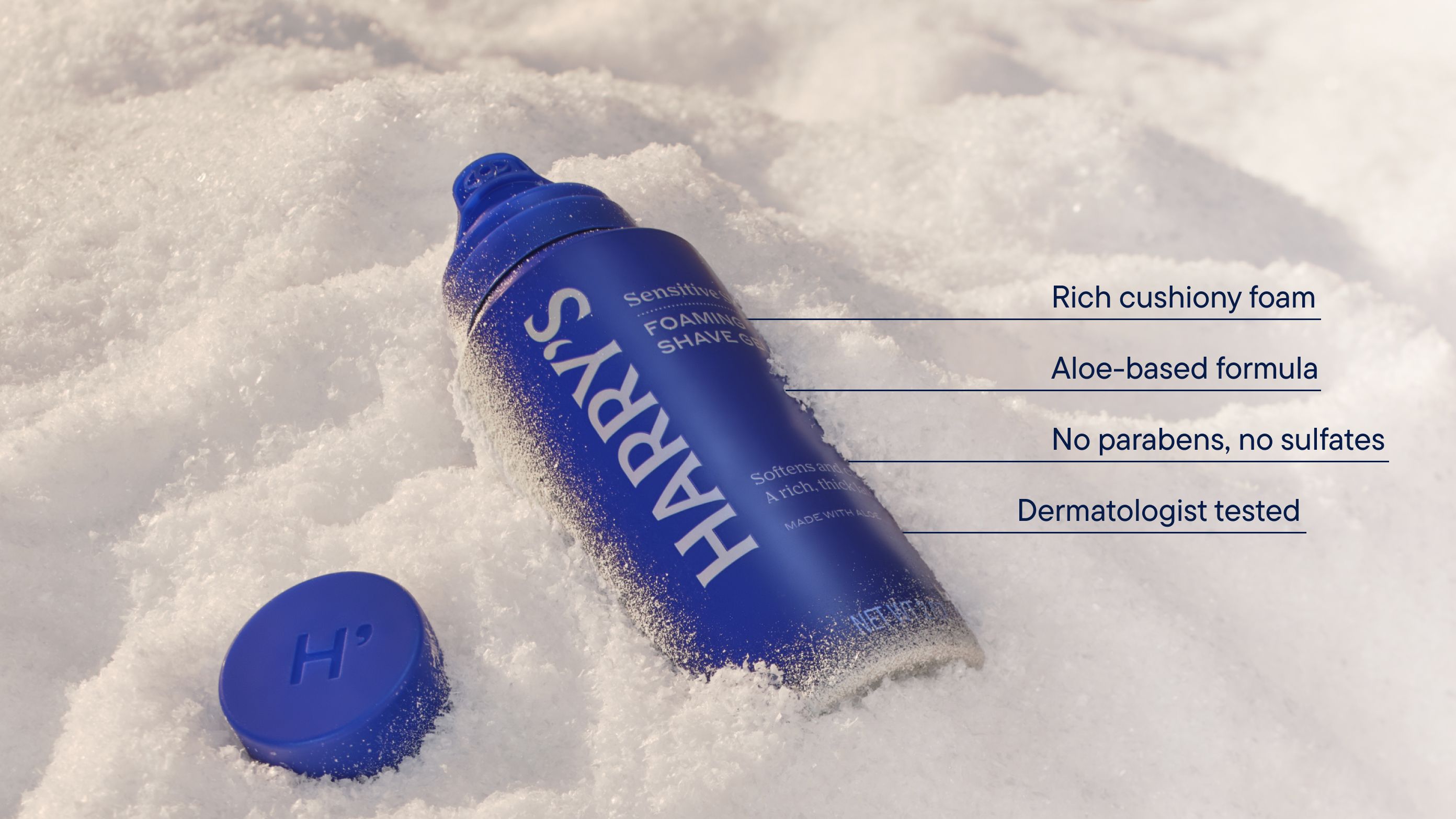A blue can of Foaming Shave Gel with the cap off in a bank of snow with text describing how it has cushiony foam, aloe-based formula, and is dermatologist tested