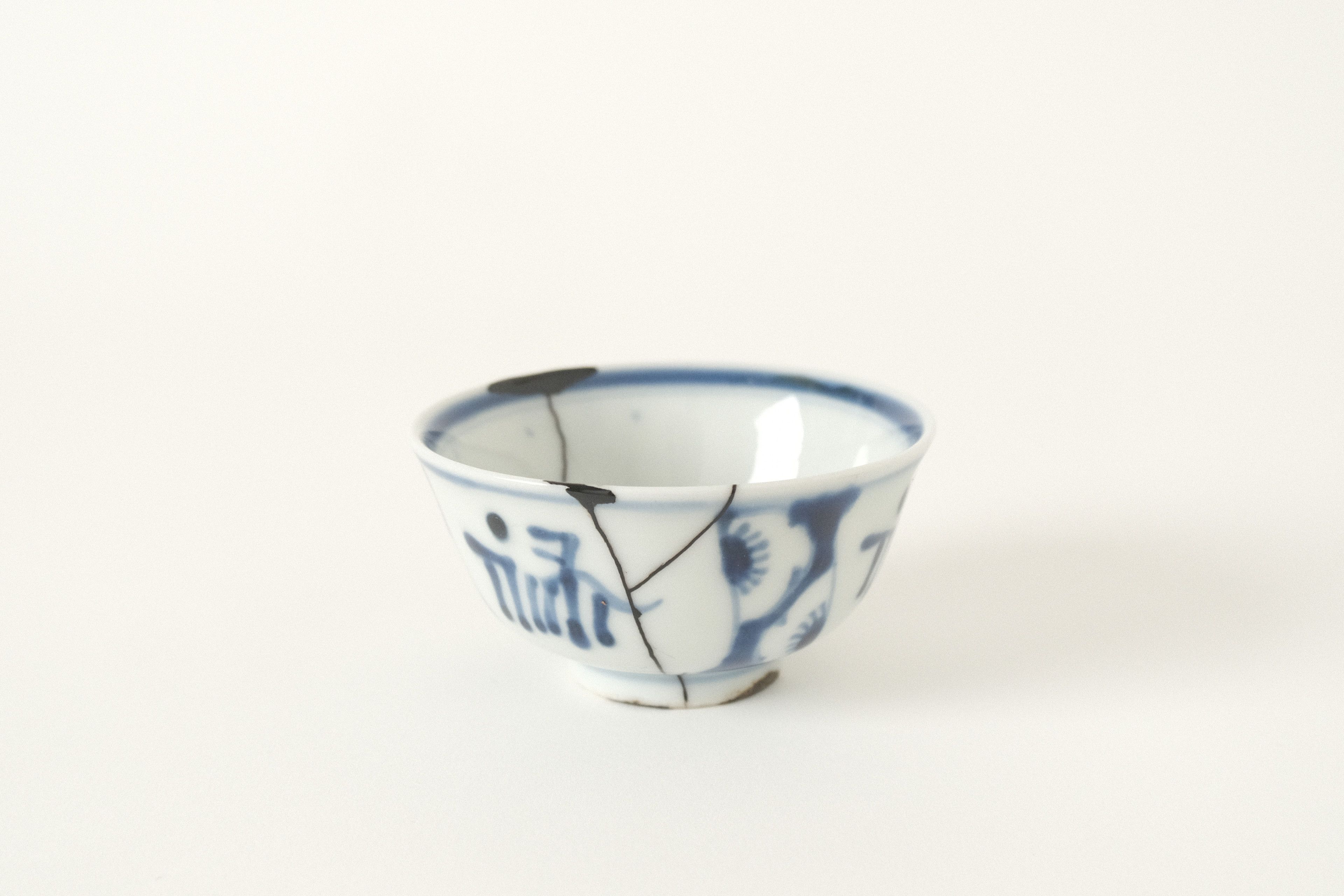 A white porcelain bowl with dark kintsugi repair lines on an off-white studio background.