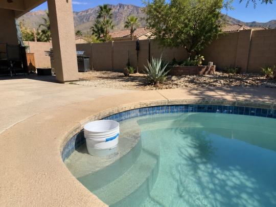 Centennial Hills Las Vegas backyard pool with a low water line and a bucket test on the top step, dry desert mountains behind.