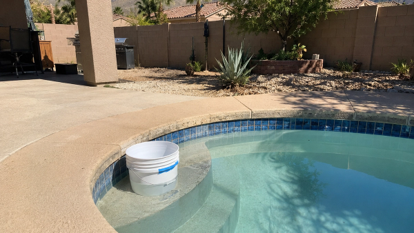 Centennial Hills Las Vegas backyard pool with a low water line and a bucket test on the top step, dry desert mountains behind.
