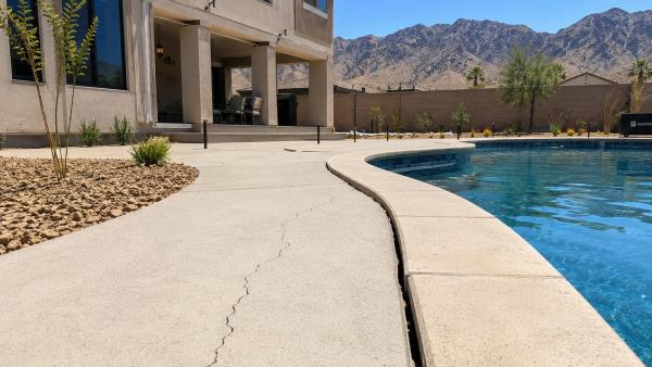 A clear, late-morning photo of a newer in-ground backyard pool behind a modern two-story stucco home in Enterprise, Las Vegas. Fresh desert landscaping with gravel and young plants.