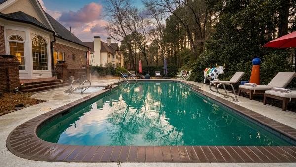 A wide shot of an upscale wooded Buckhead backyard pool right after a heavy summer storm, with clearing dark clouds, a visibly wet deck and clay soil, and puddles near the pool edge.