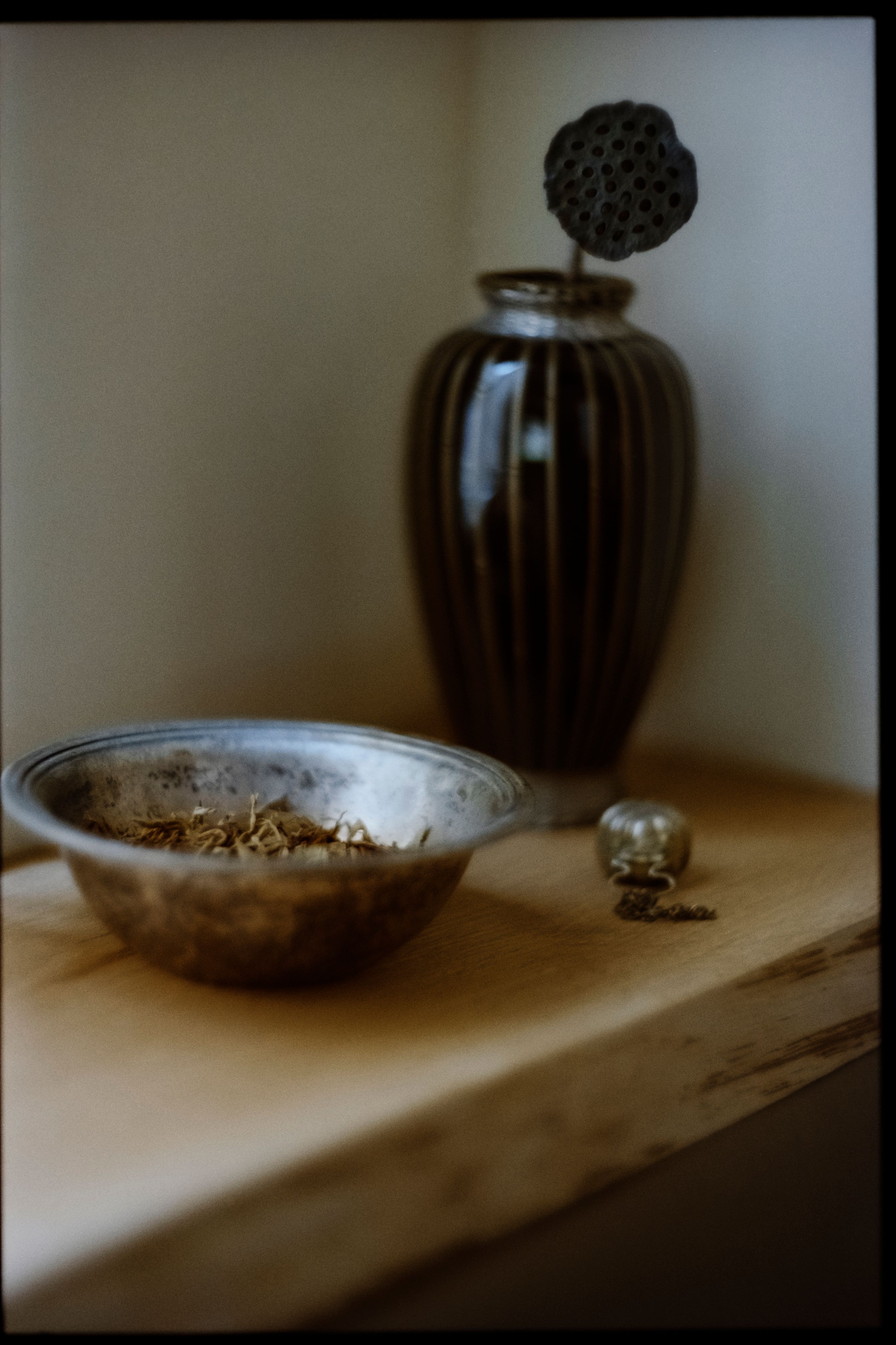 a silver bowl with pot pouri in it, a black vase with a dried flower in it, WOE, Width Over Ears