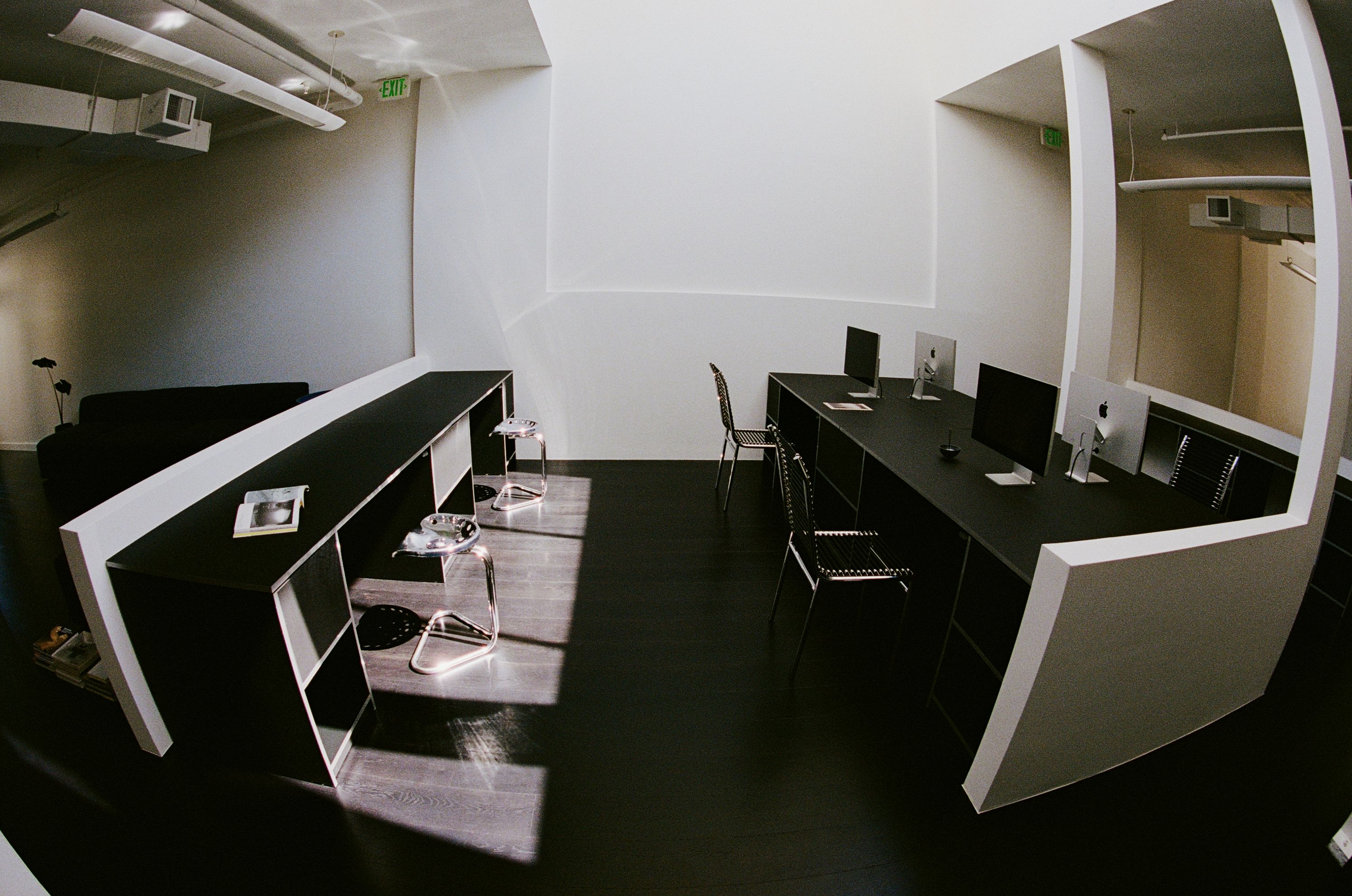 a room with long black desks, metal stools, and bungee cord chairs