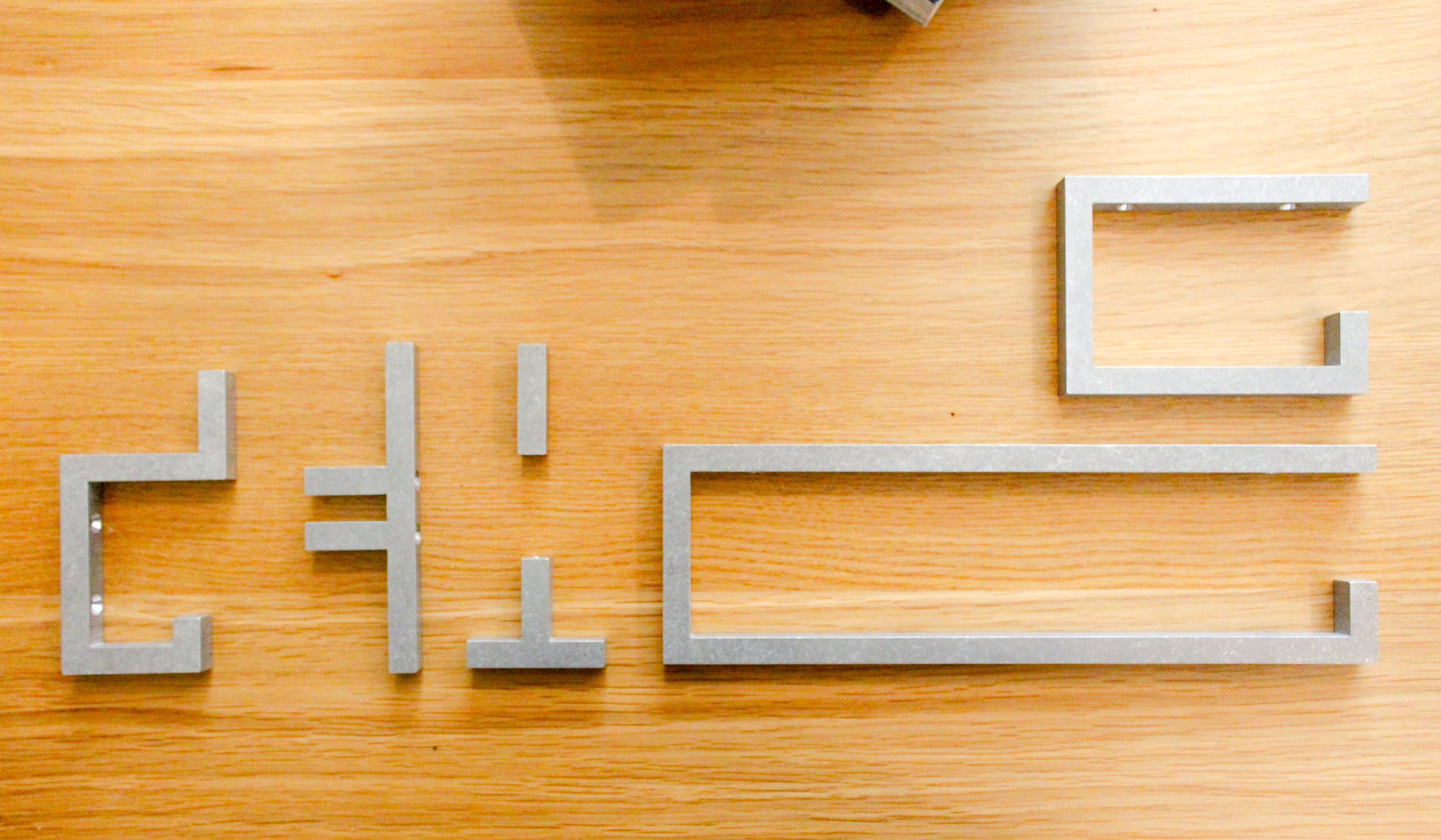A selection of machined, tumbled aluminum hardware pieces on an oak table, Preston Taylor Alba, WOE, Width Over Ears
