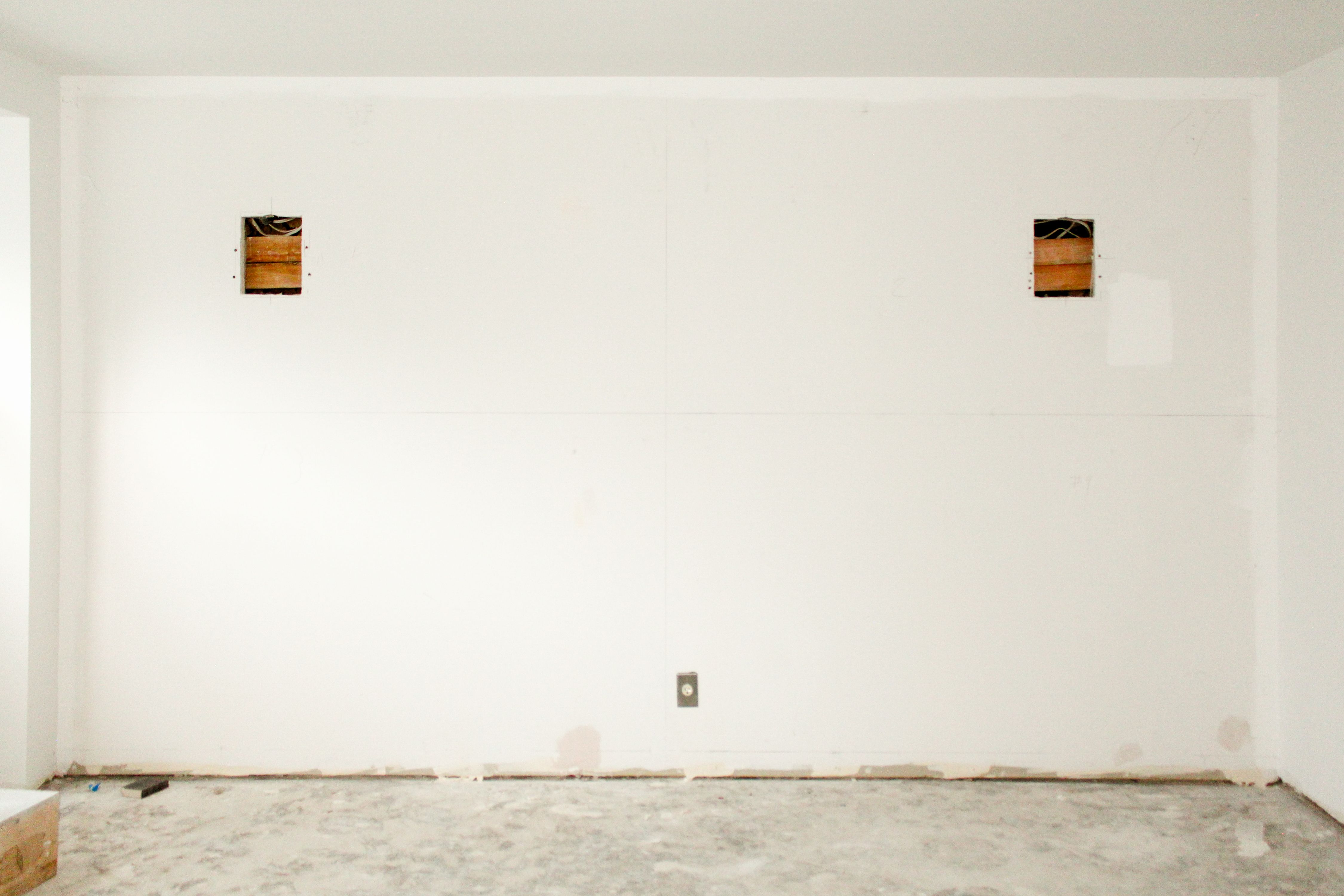 a construction site with a man holding up a light fixture against a blank wall, WOE, Width Over Ears