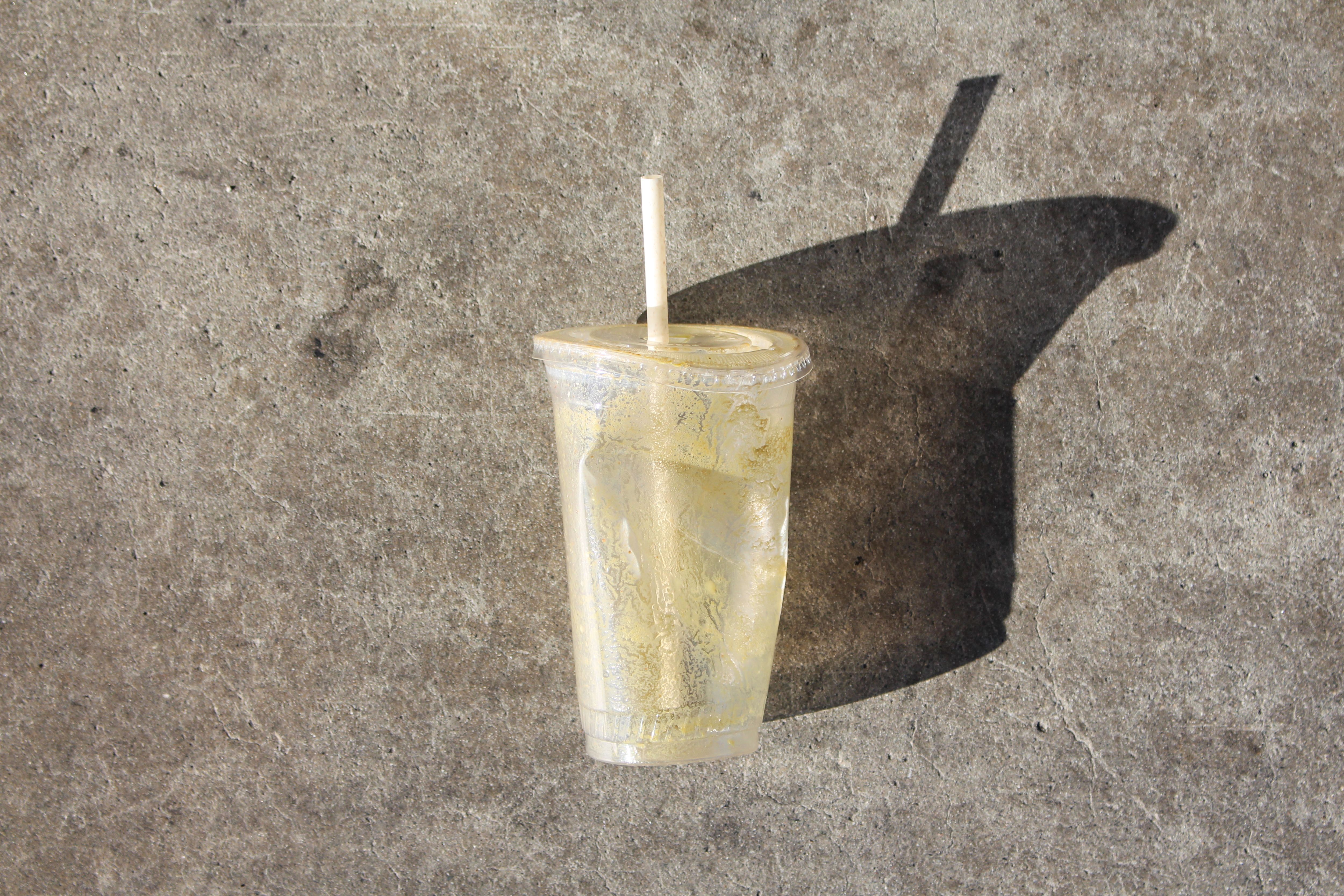 a crushed plastic cup on the ground with long shadow, WOE, Width Over Ears