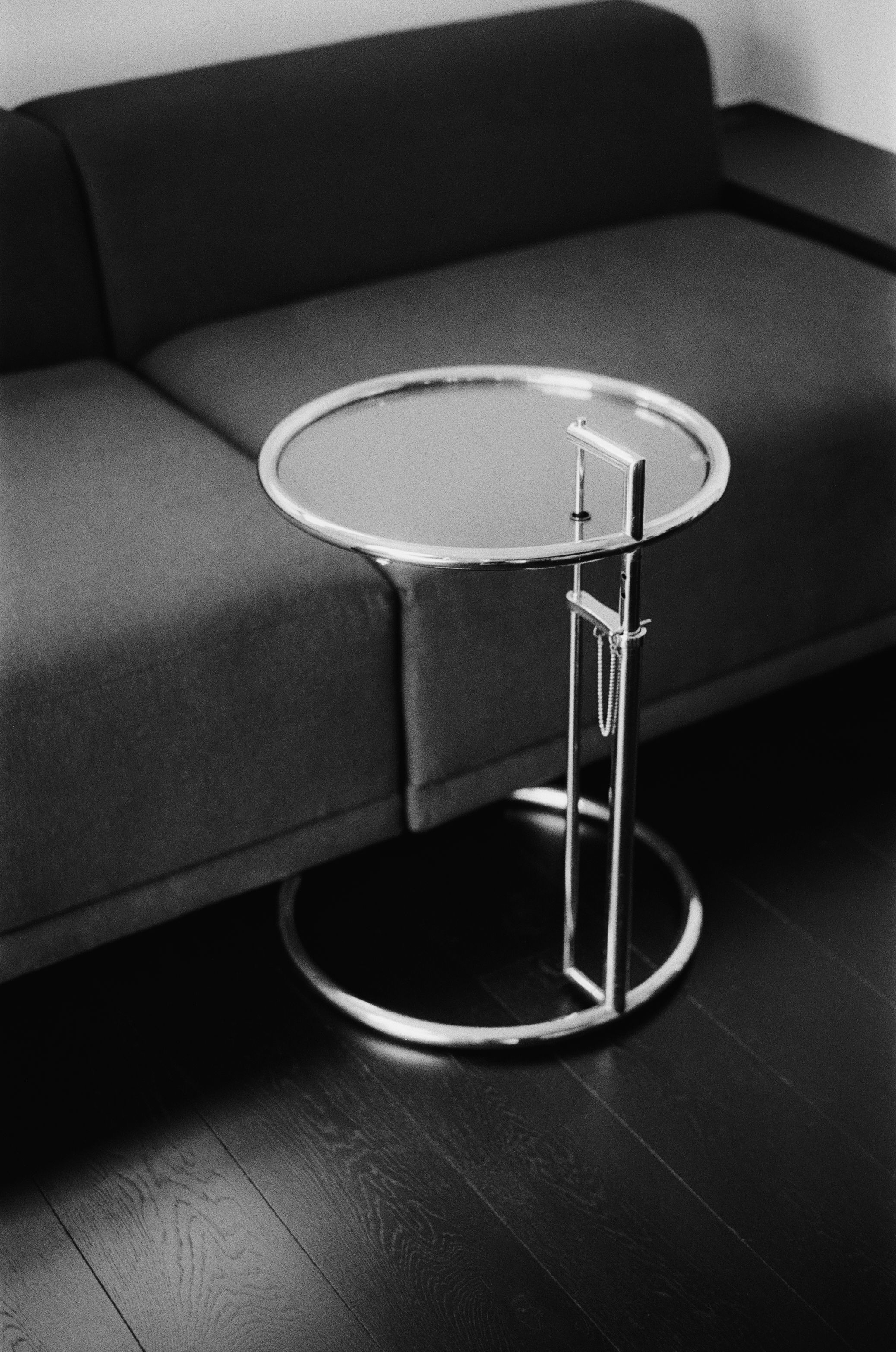 a black and white image of round chrome and glass table nesting with a sofa