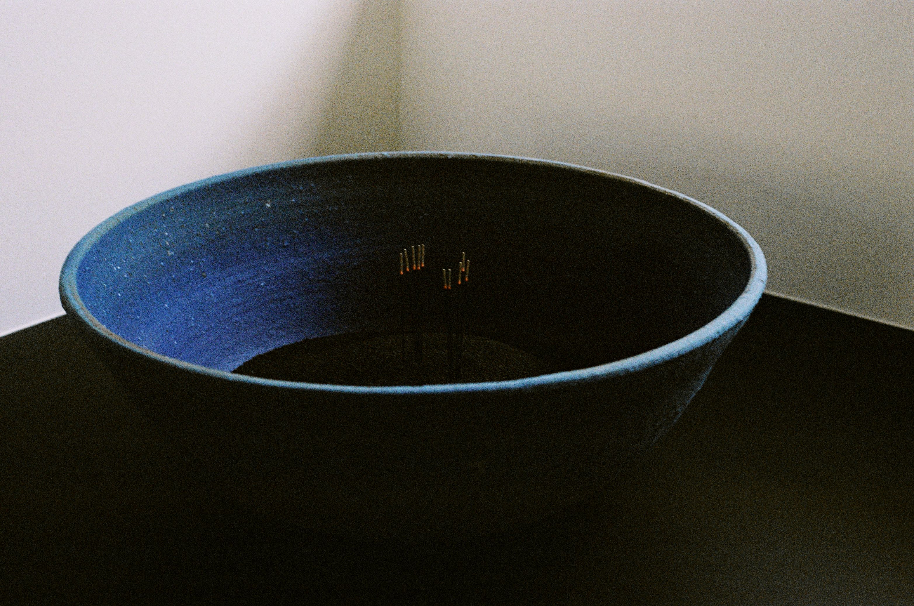 a blue bowl with black sand in it and incense burning in the sand