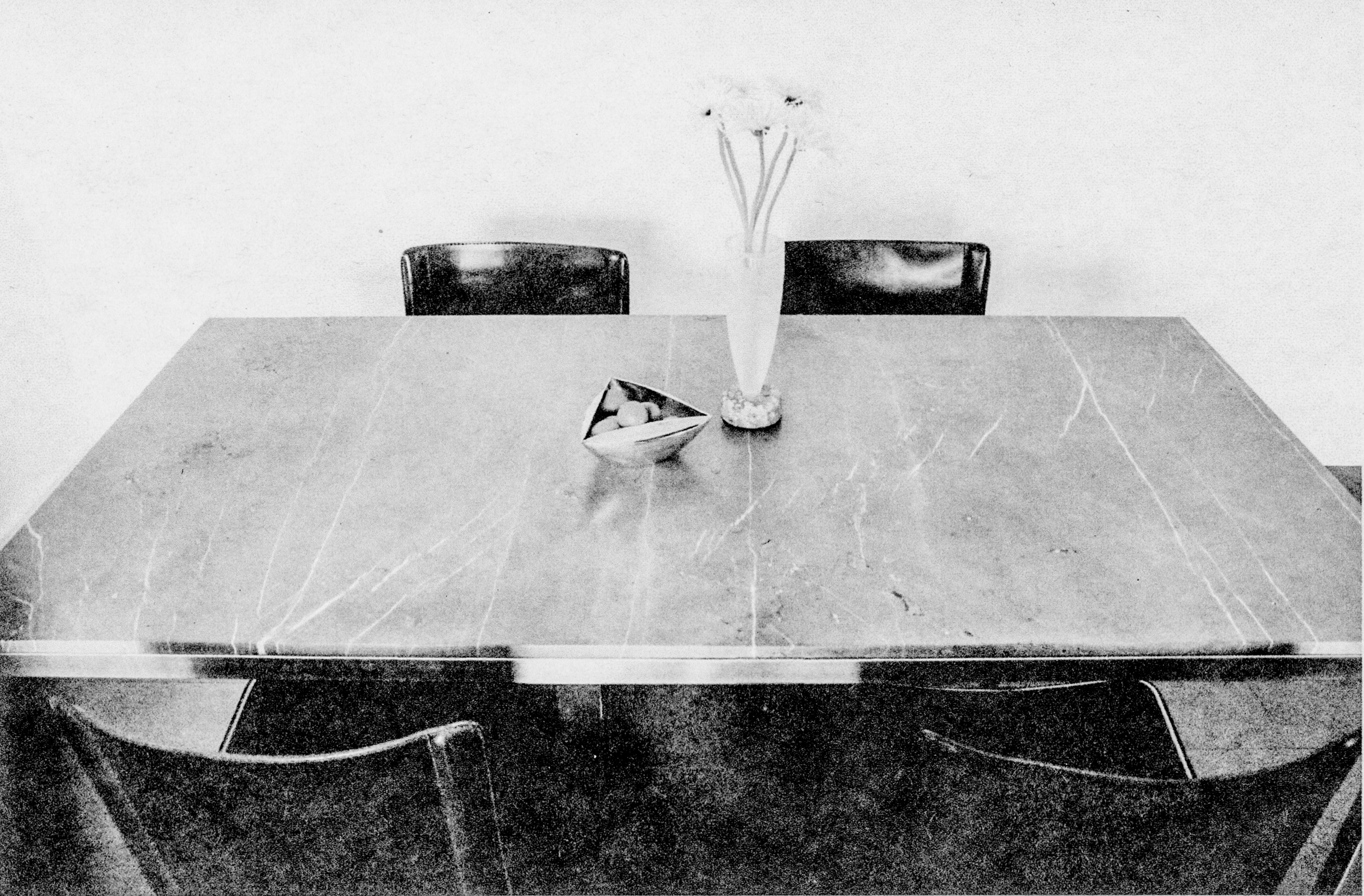 black and white image of a marble table top with four black chairs and a vase