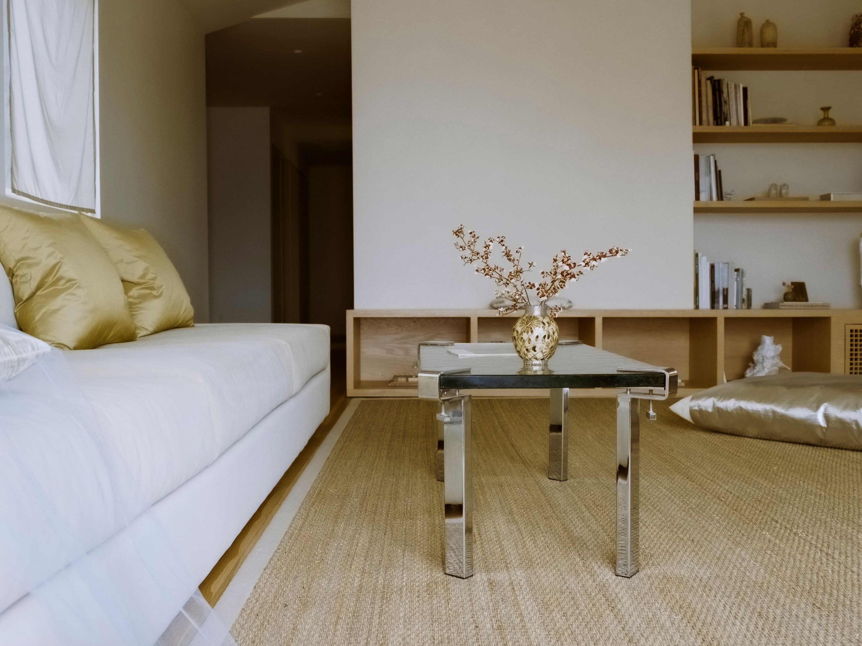 a coffee table with glass top and silver legs next to a light green velvet sofa, woe, width over ears
