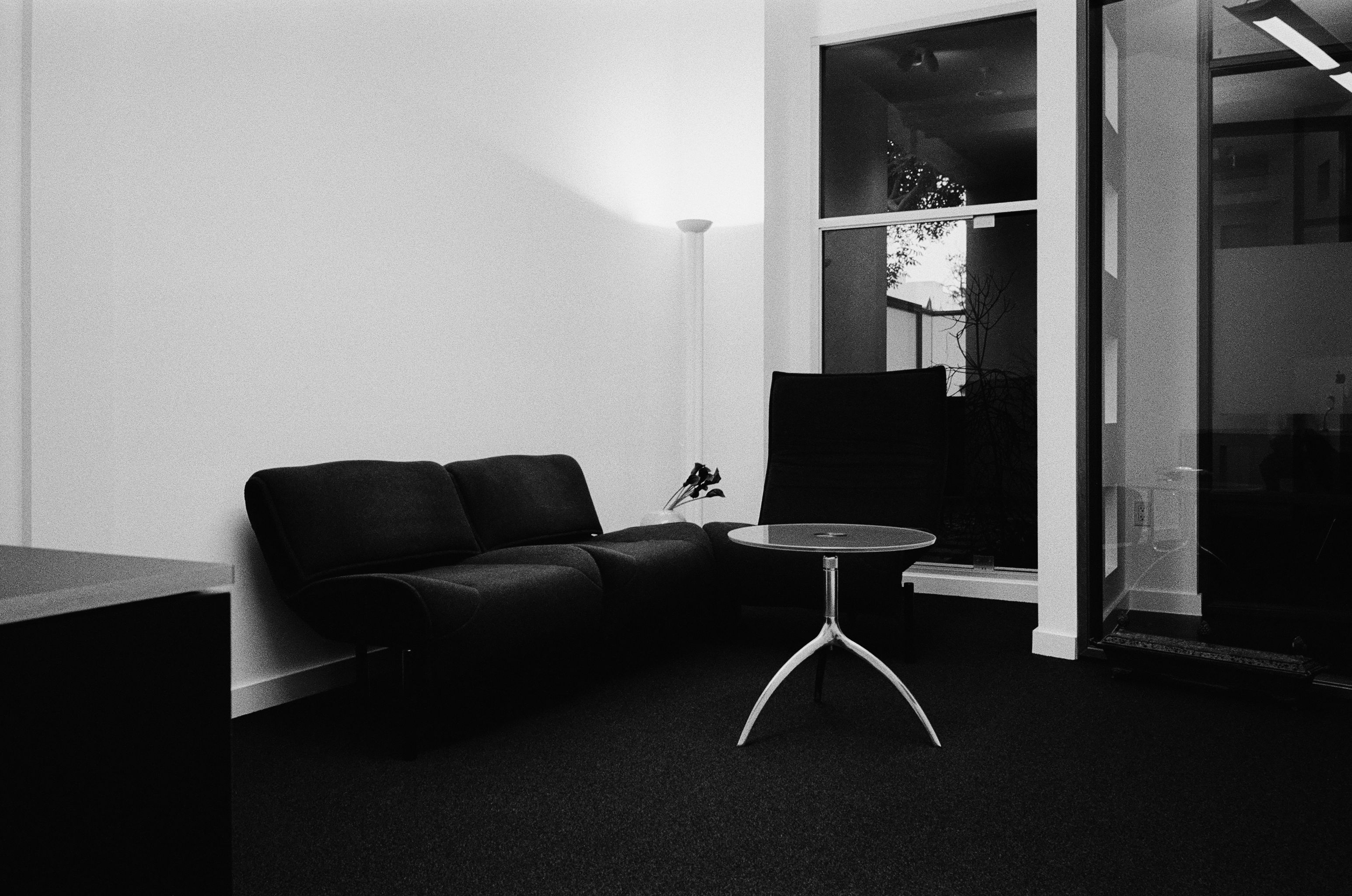 a black and white image of an office with a dark sofa, metal and glass coffee table 