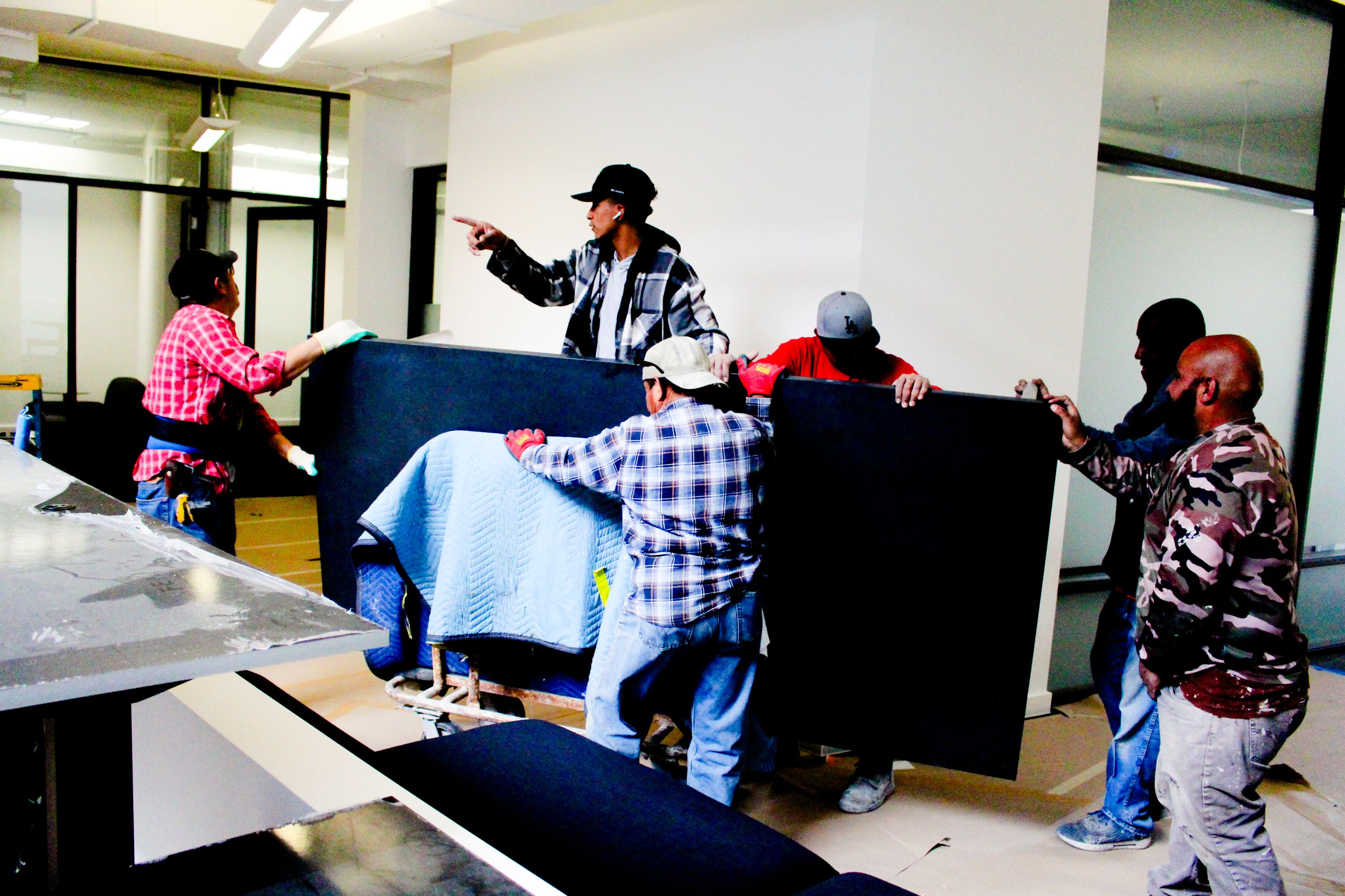 a group of men pushing a large rectangular stone table top through an office space