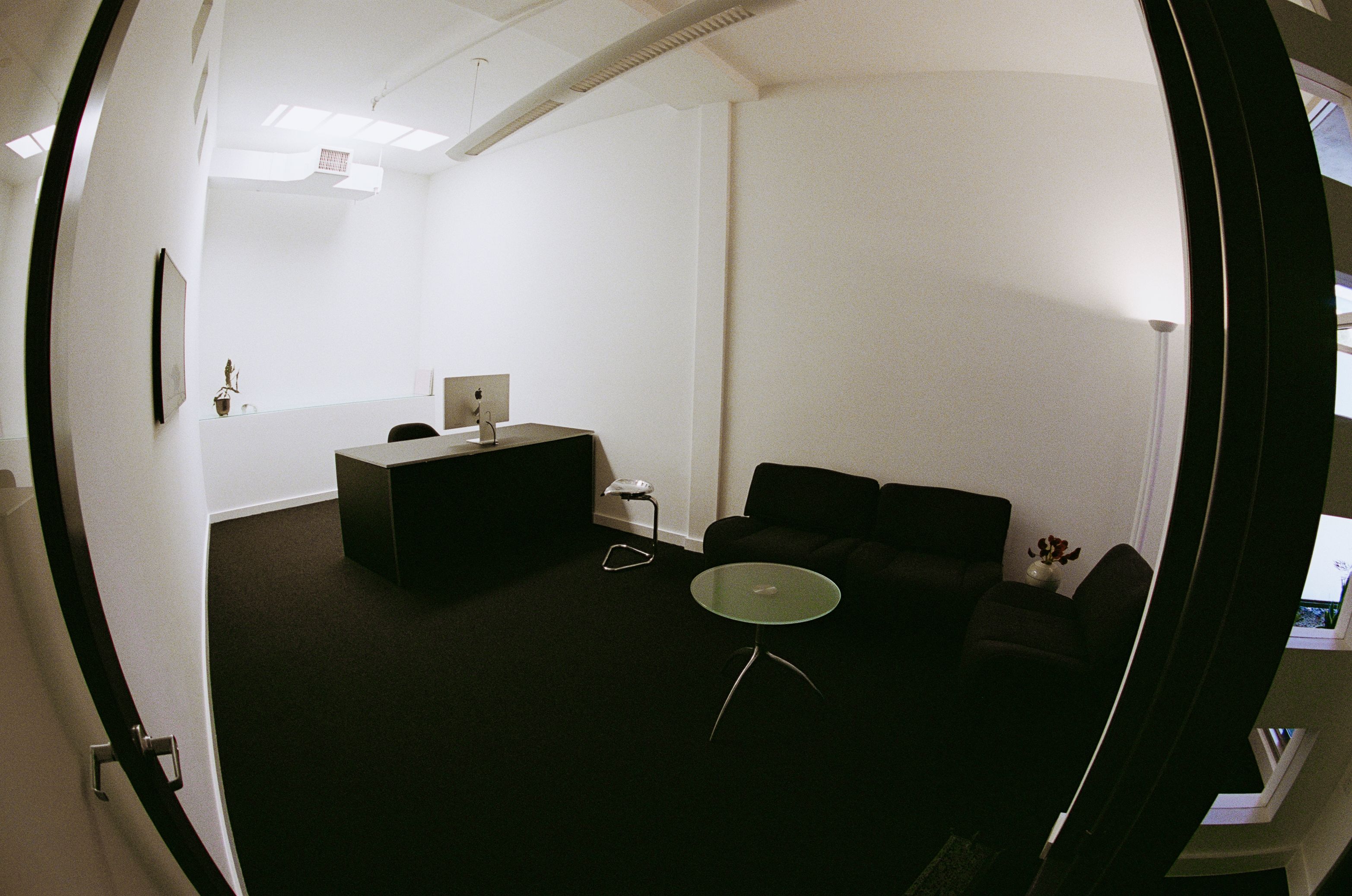 an office with glass coffee table, metal stool, and black desk, with skylight above