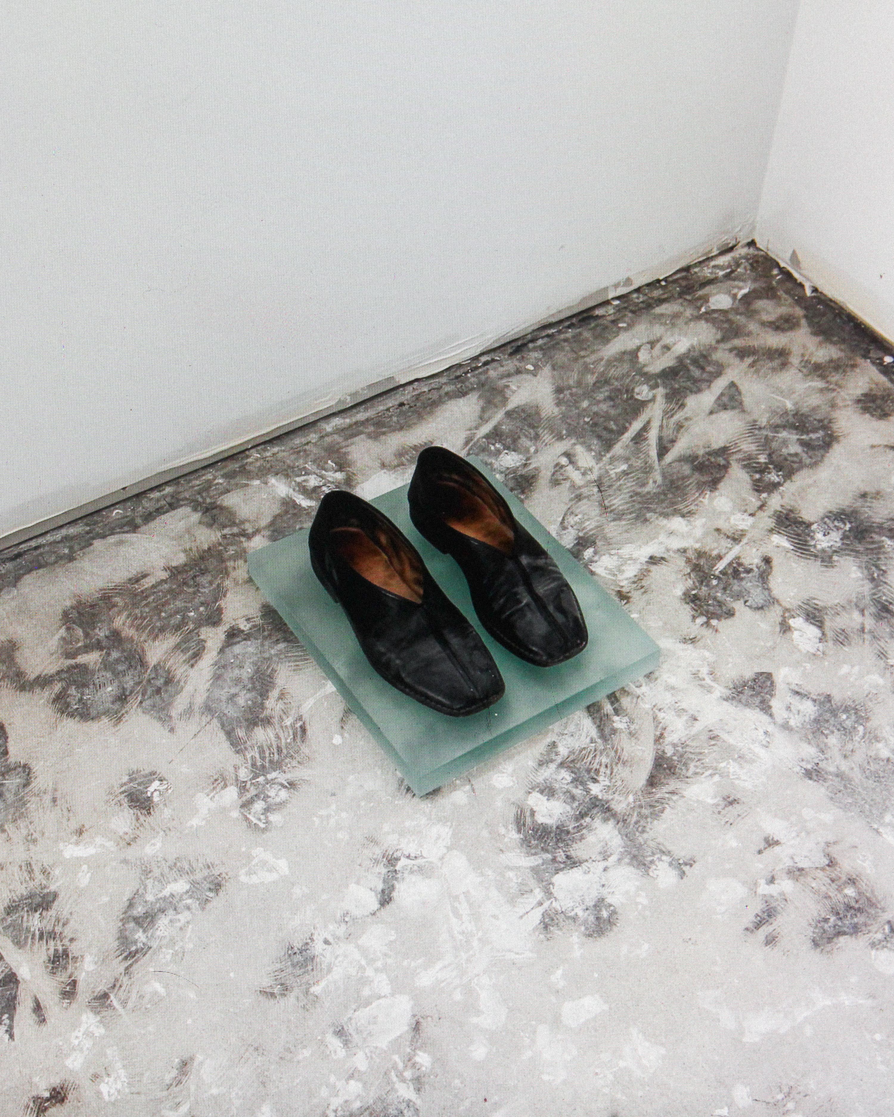 a pair of black shoes on a green piece of material on a dirty concrete floor, WOE, Width Over Ears